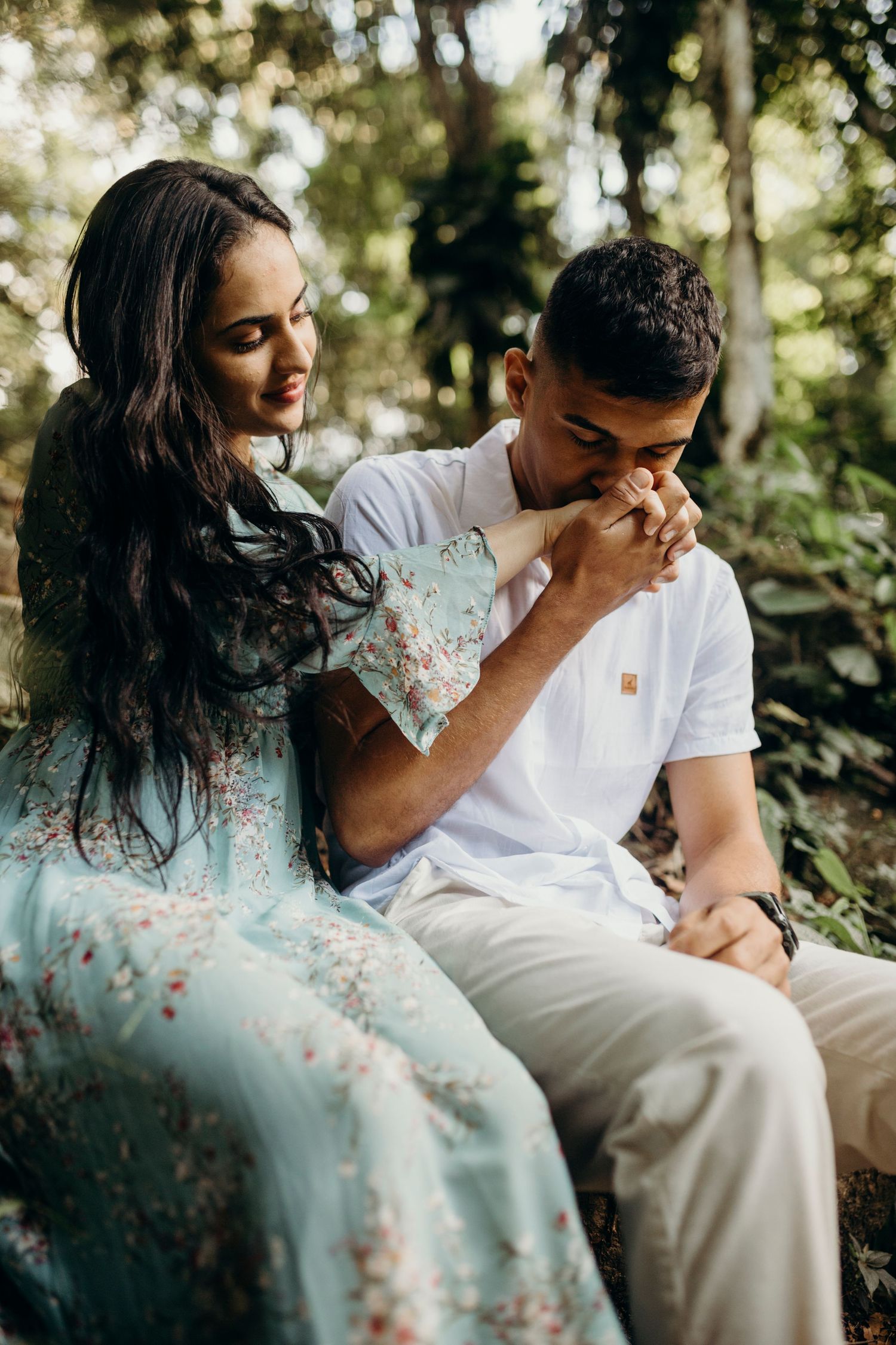 Couple sharing emotional moment on stone steps surrounded by forest foliage.