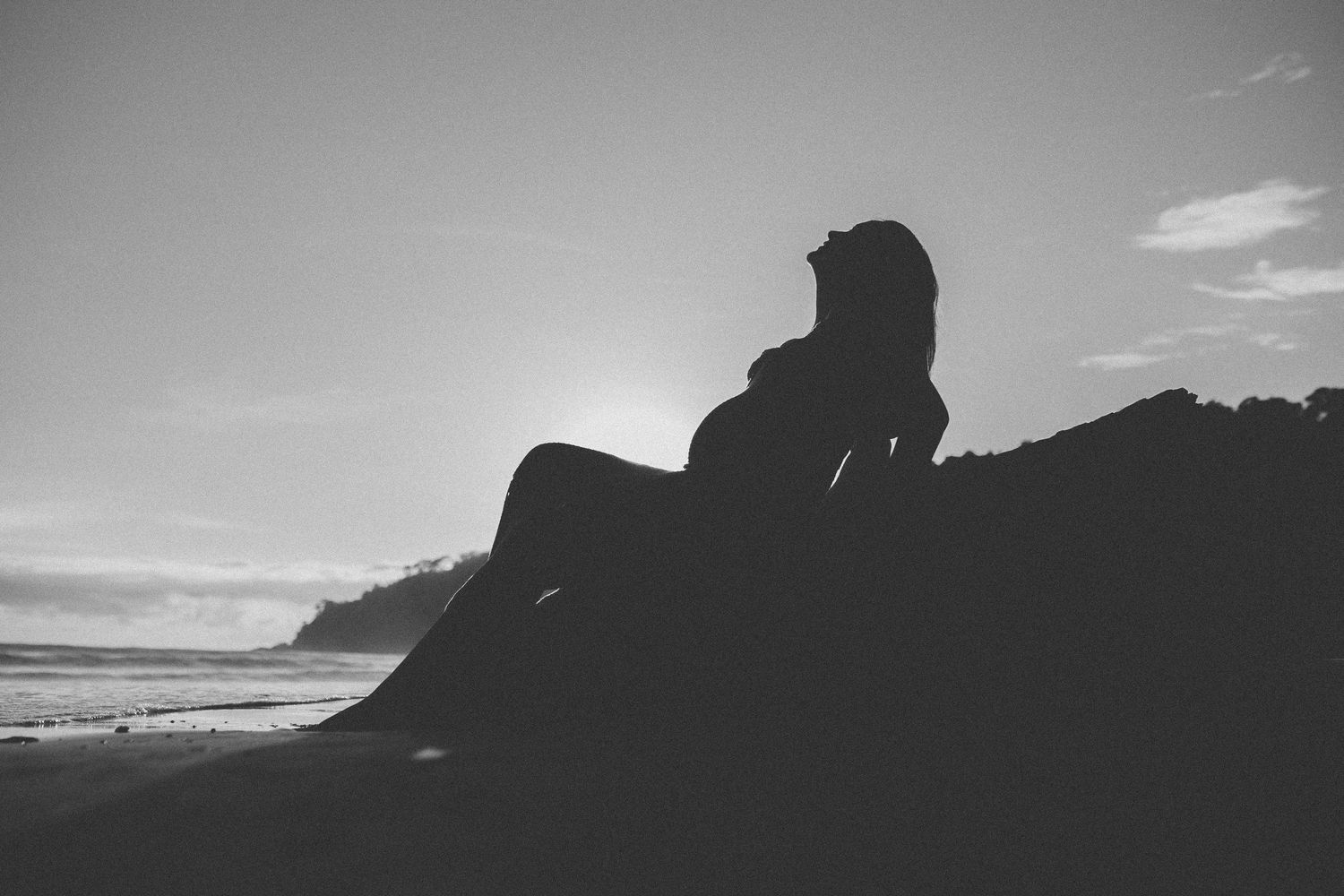 Dramatic black and white silhouette of coastline and cliffs against cloudy sky.