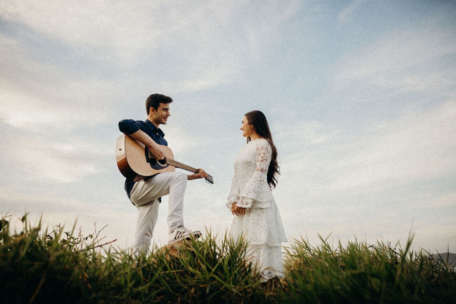 A couple shares a musical moment on a grassy hilltop overlooking the ocean.