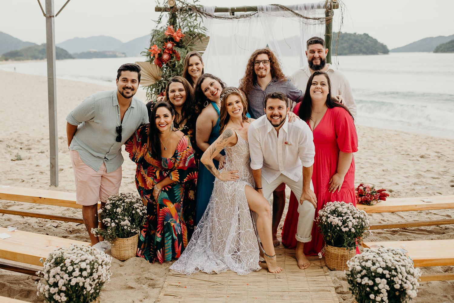 Wedding party group photo on a beach with an ocean view and floral decorations.