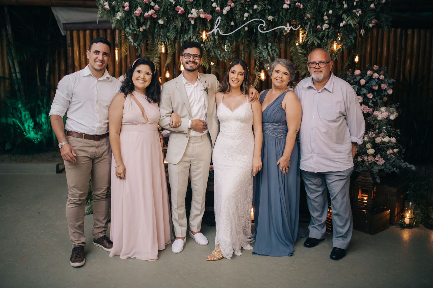 Wedding celebration group photo with attendants in blush and blue attire against floral backdrop.