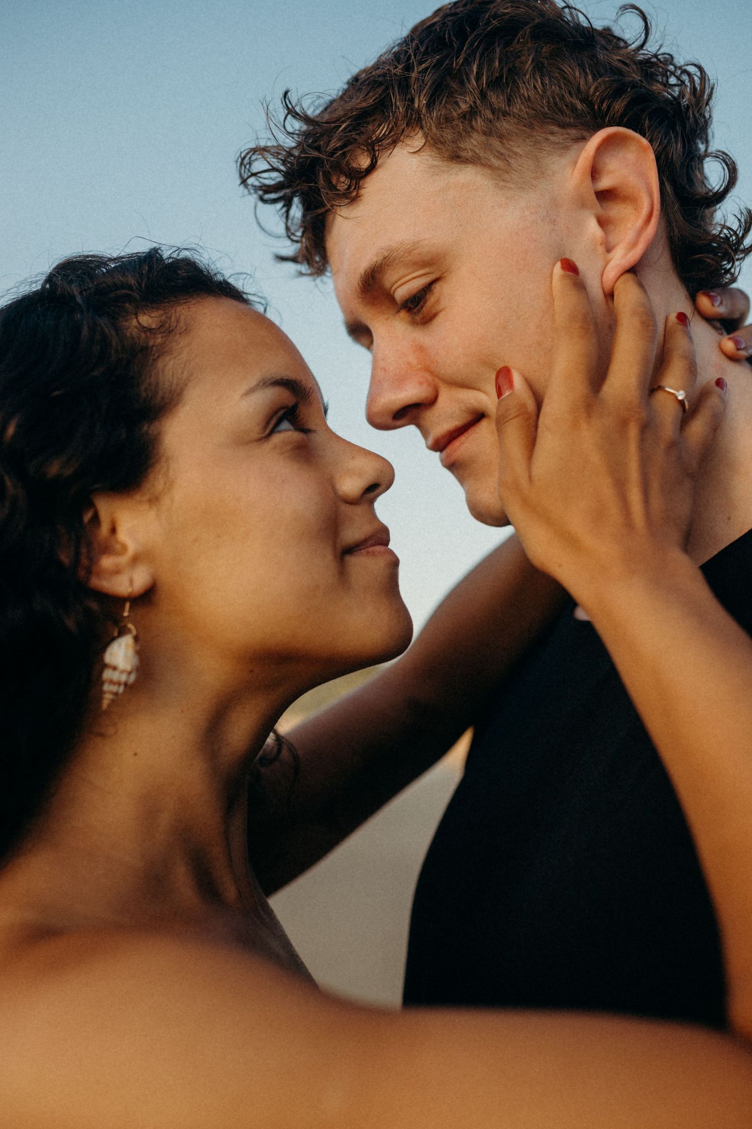 Intimate close-up of a couple sharing a tender moment against a sunset sky.