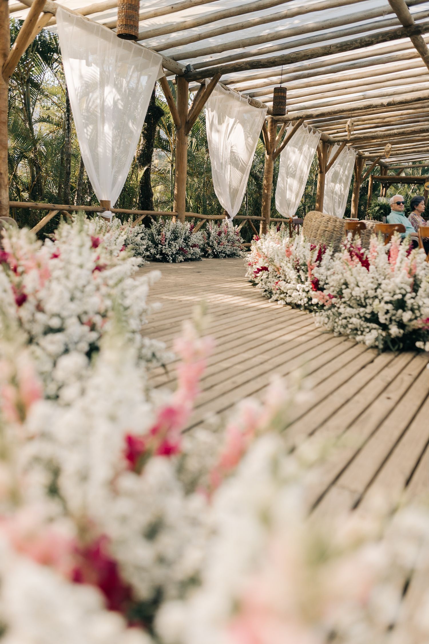 Beautiful floral arrangements line a covered outdoor wedding venue with white draping.