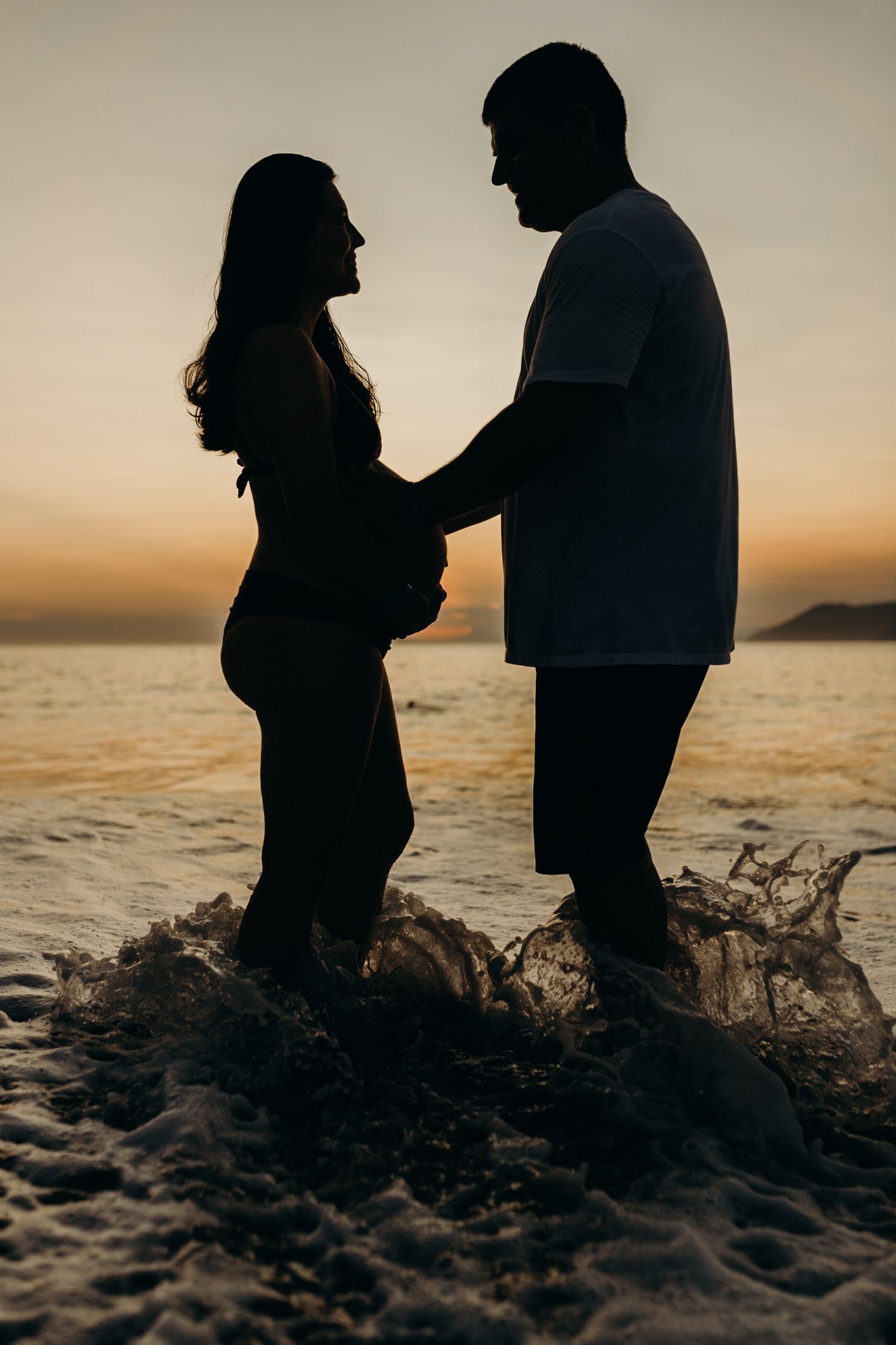 Silhouetted couple sharing an intimate moment on the beach at golden hour.