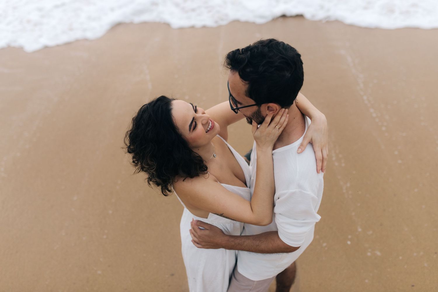 A couple shares an intimate moment on a sandy beach during golden hour.
