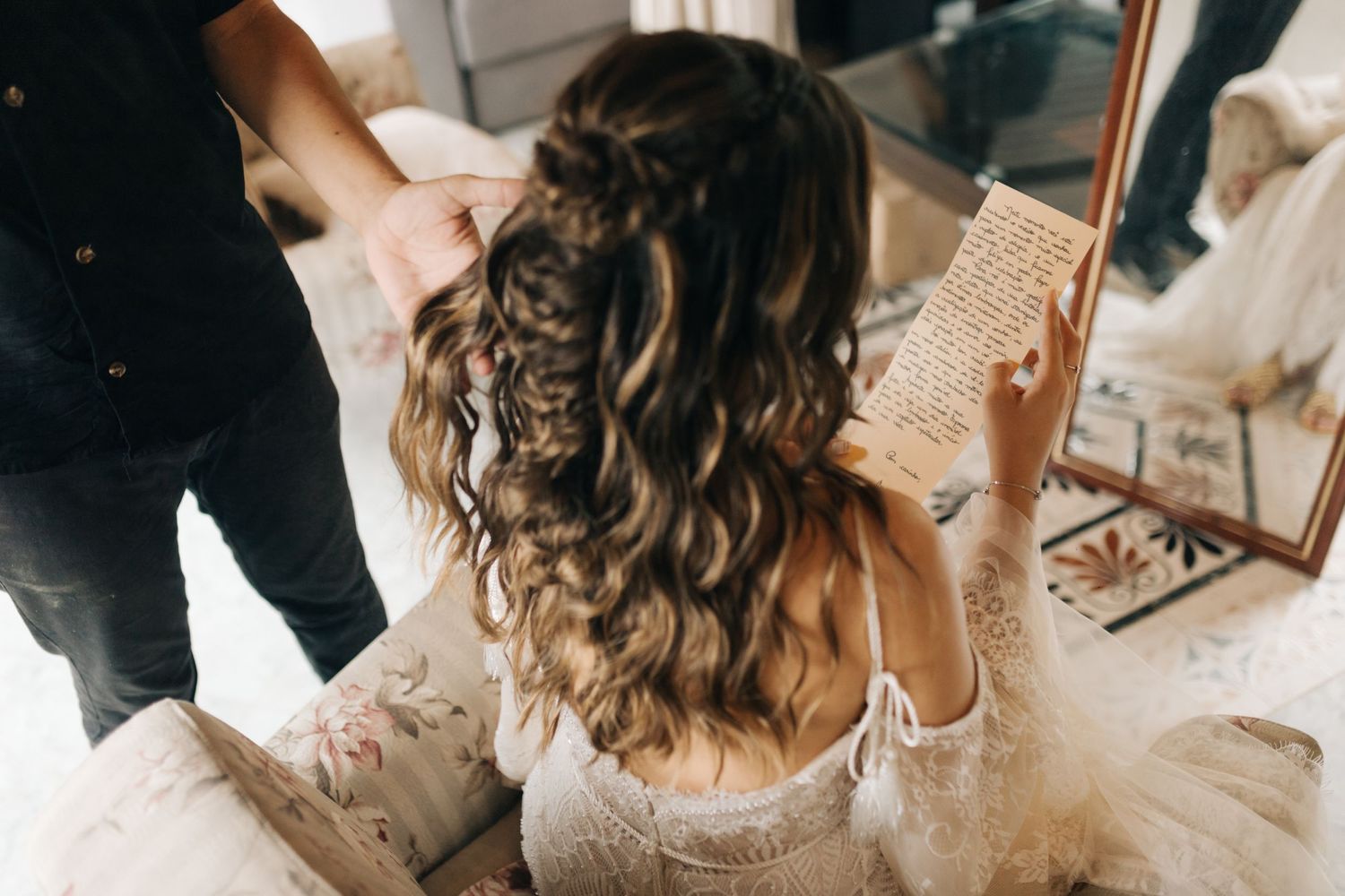 Back view of long curled hair and white lace wedding dress details.