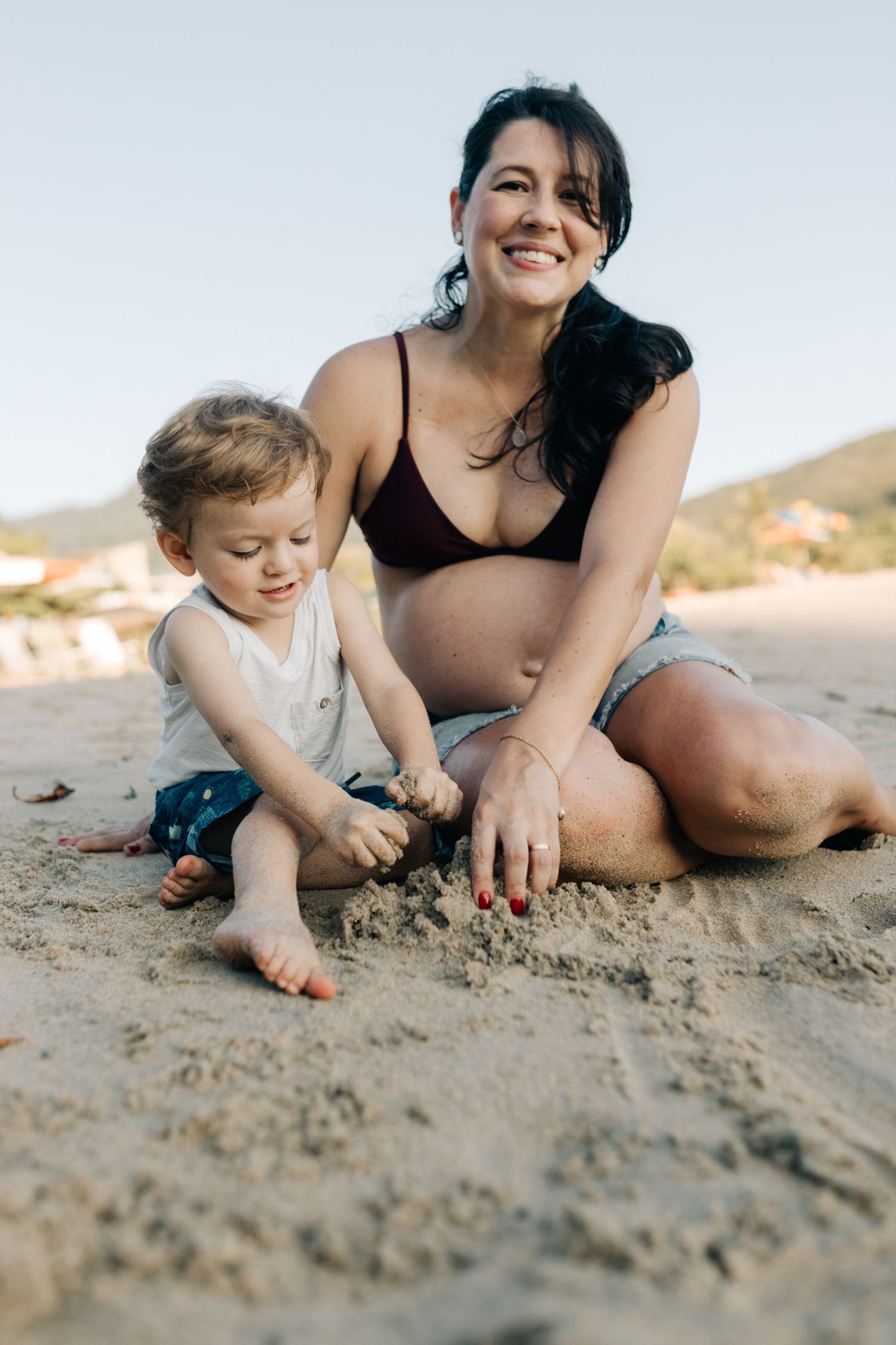 A playful beach scene shows a tender moment of sand exploration between adult and child.
