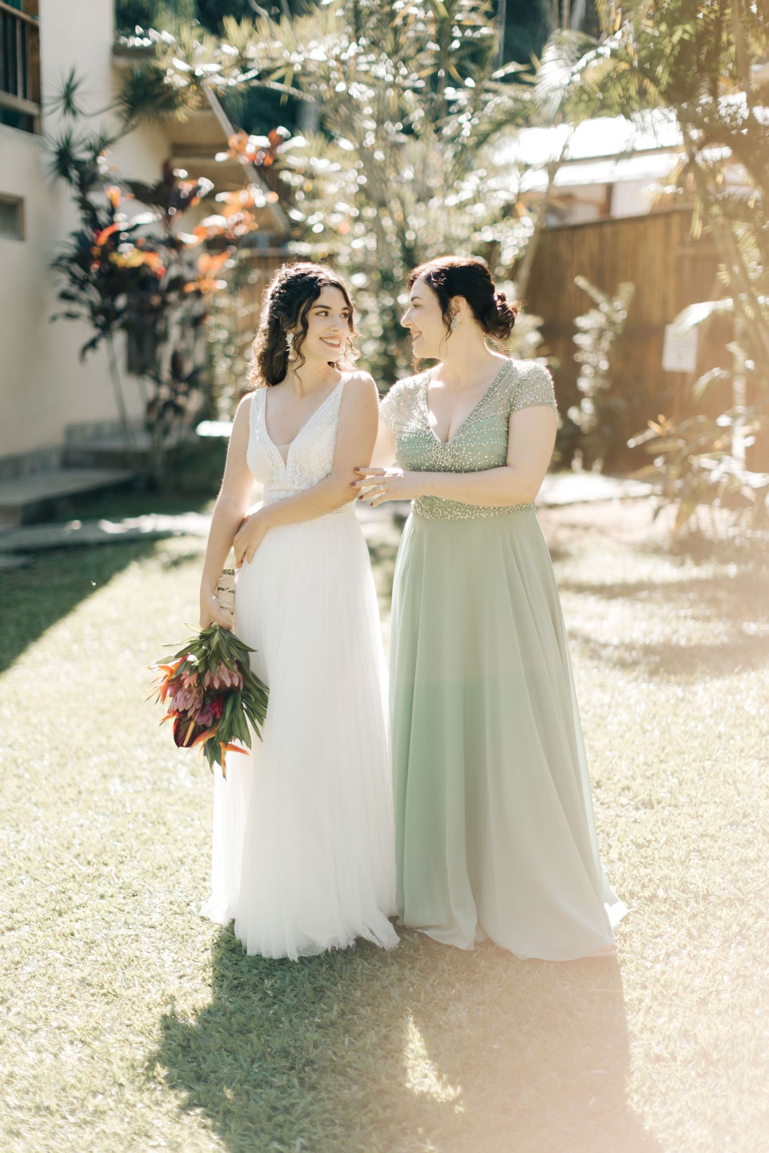Two people in formal dresses sharing a tender moment in a sun-dappled garden.