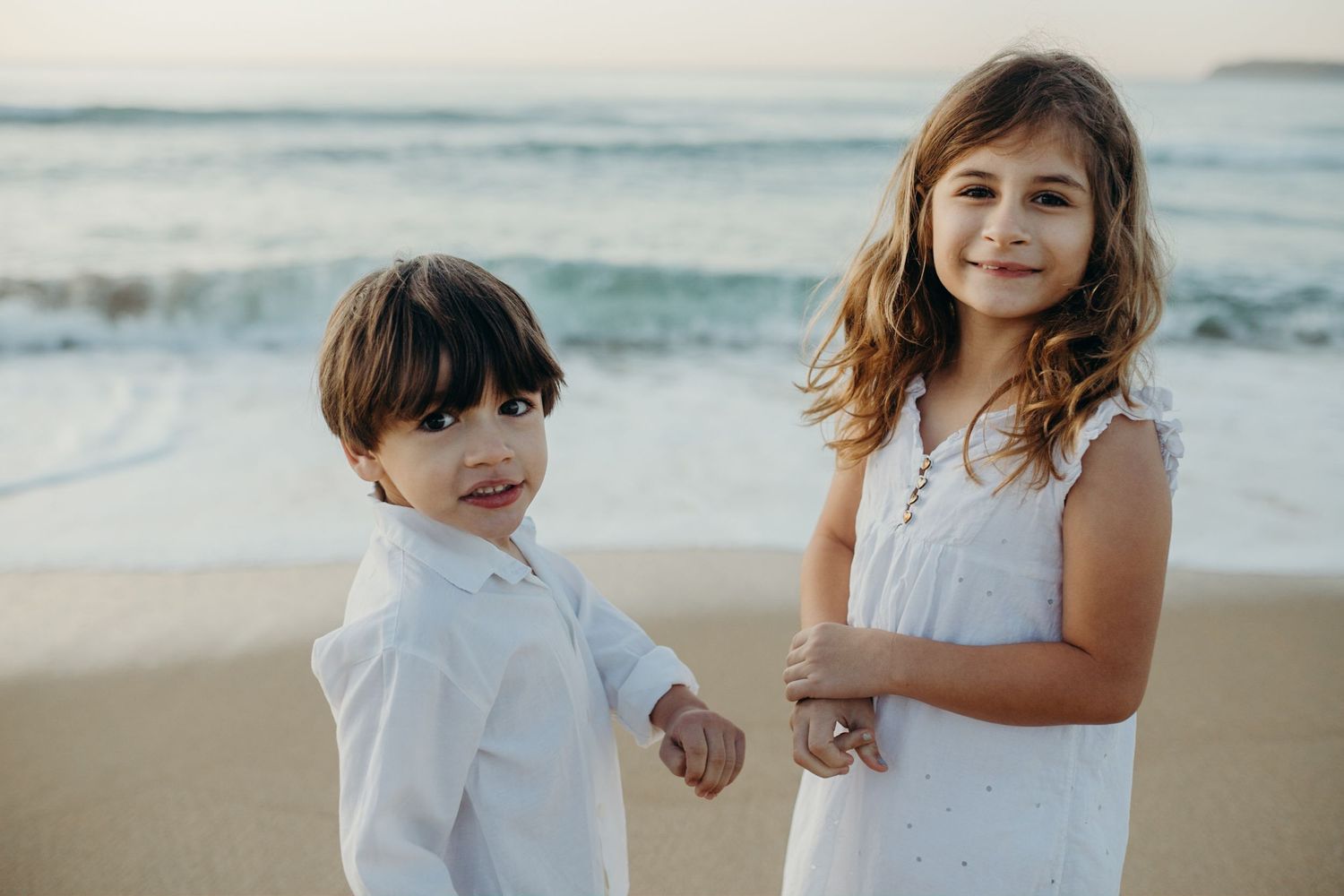 Children in white outfits playing and bonding together on a beautiful beach at sunset.