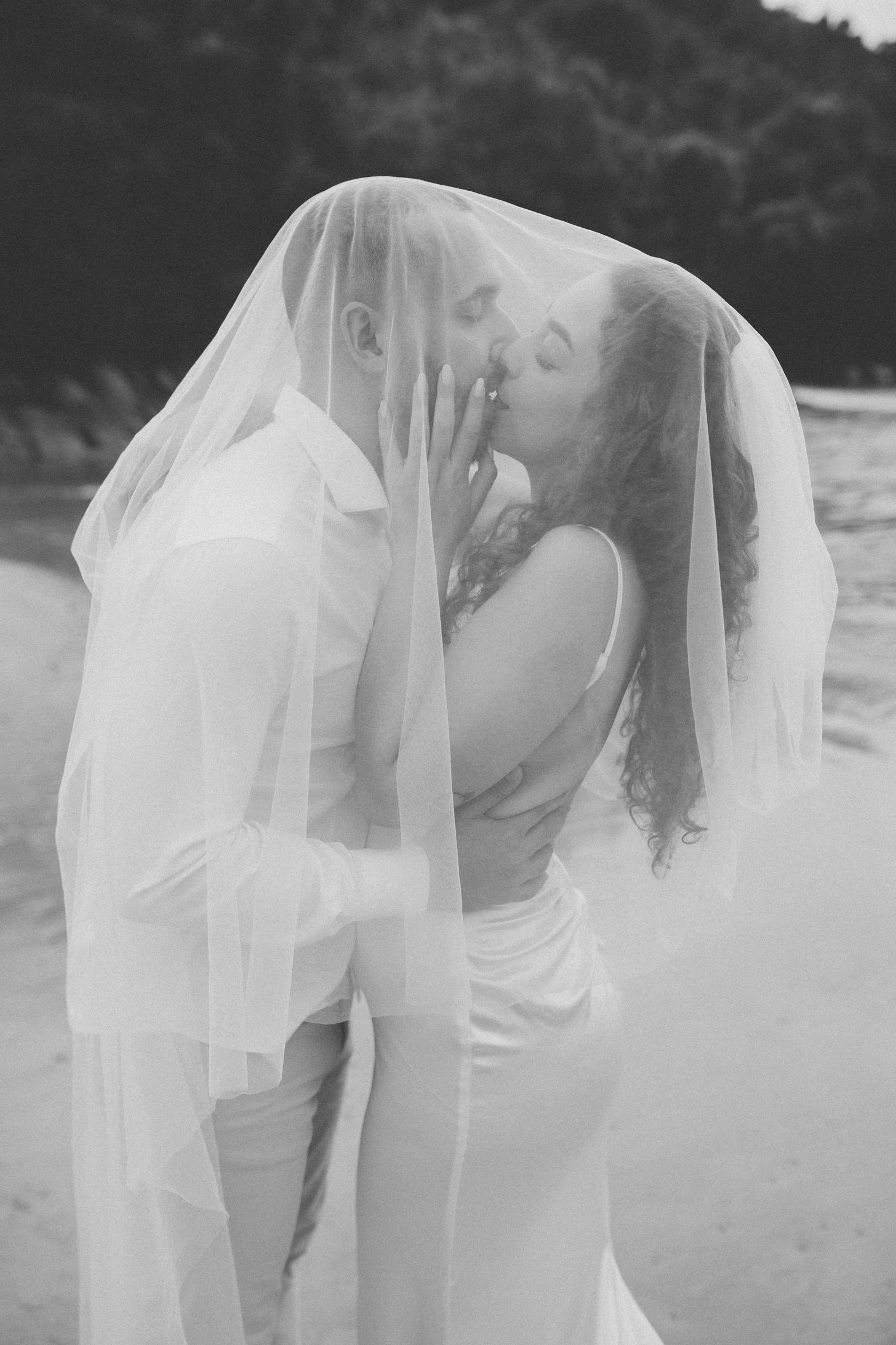Artistic black and white wedding photo with couple under flowing veil.