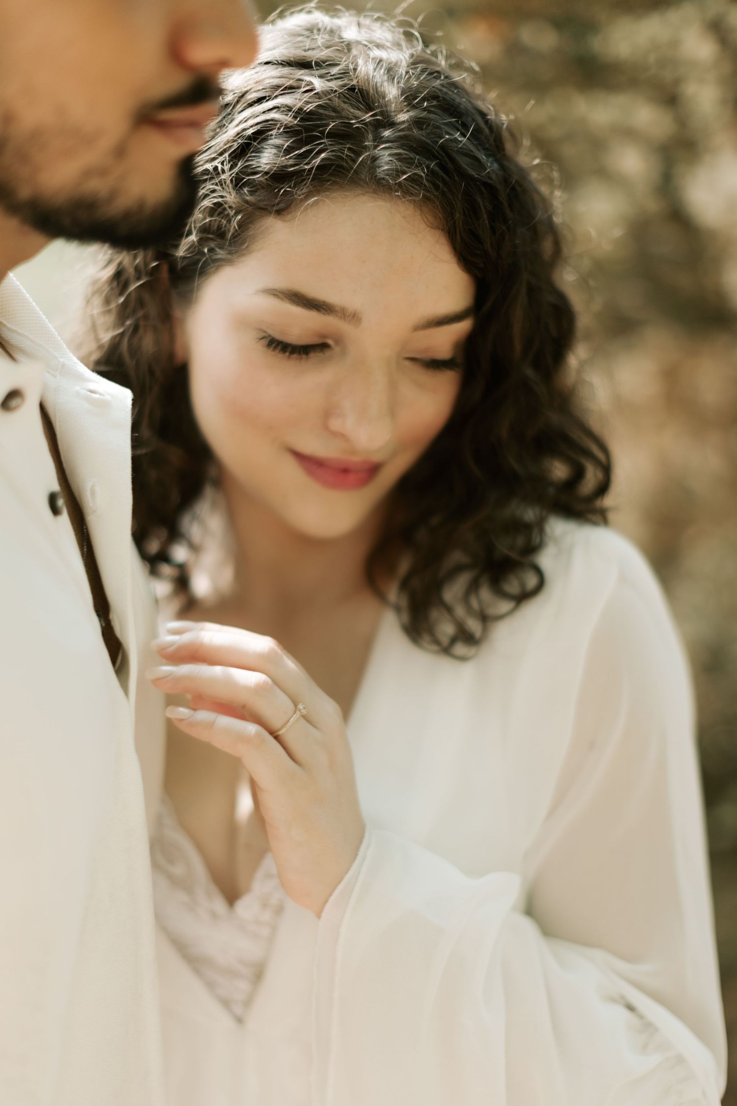 A close-up shot of a woman in white with curly hair smiling softly.