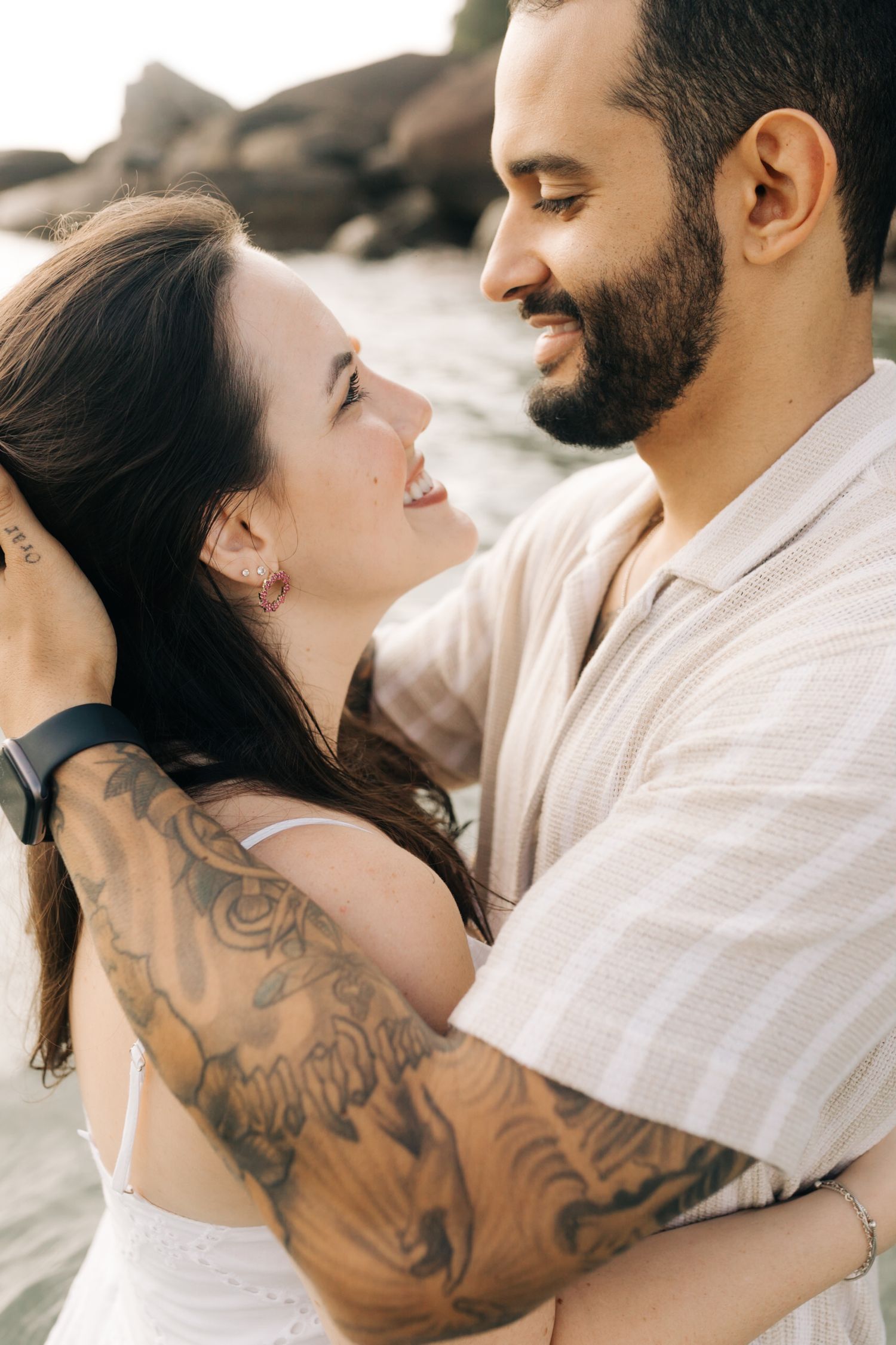 A couple in white clothing share a tender moment on the beach.