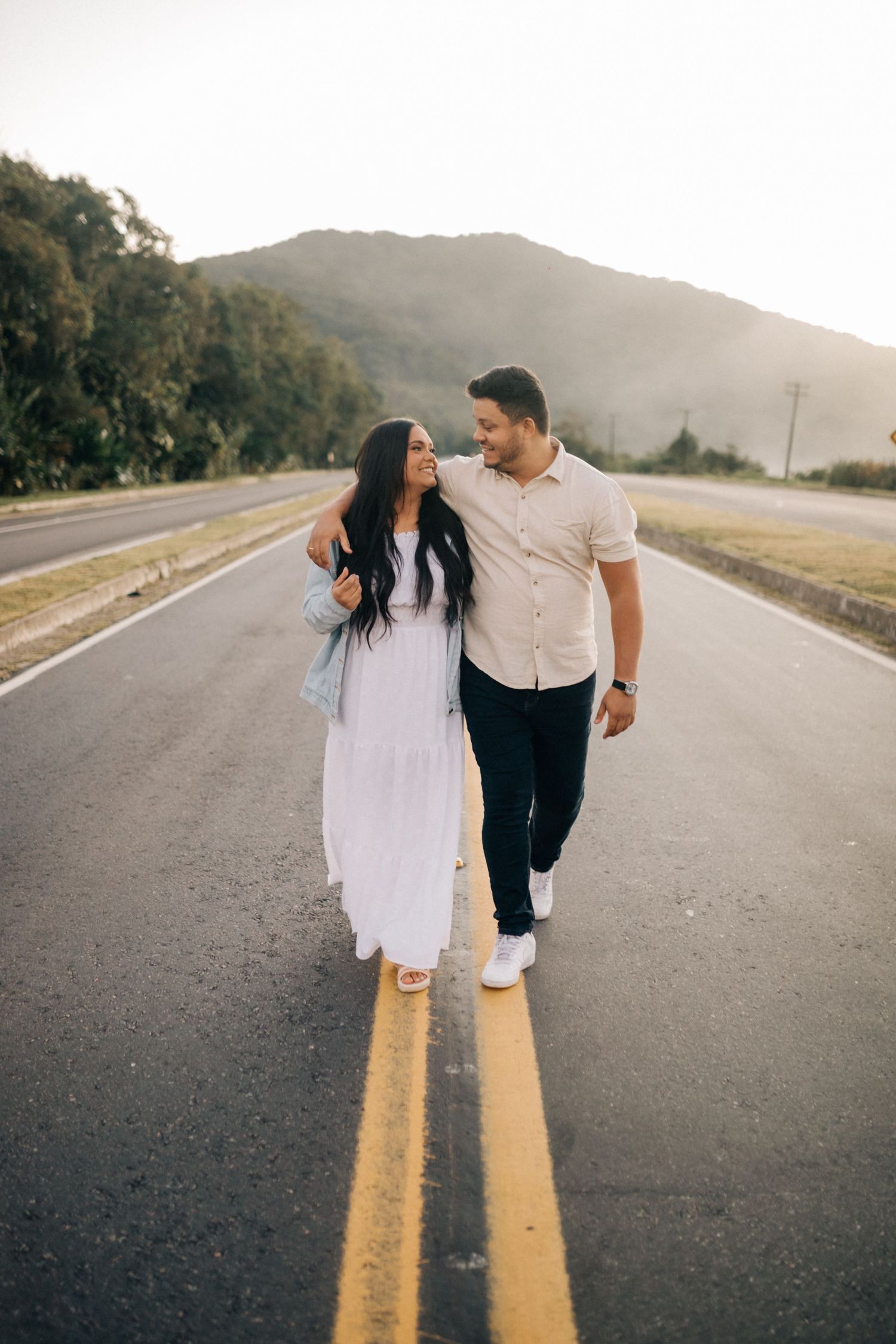 Romantic couple walking together on an empty road surrounded by mountains at sunset.