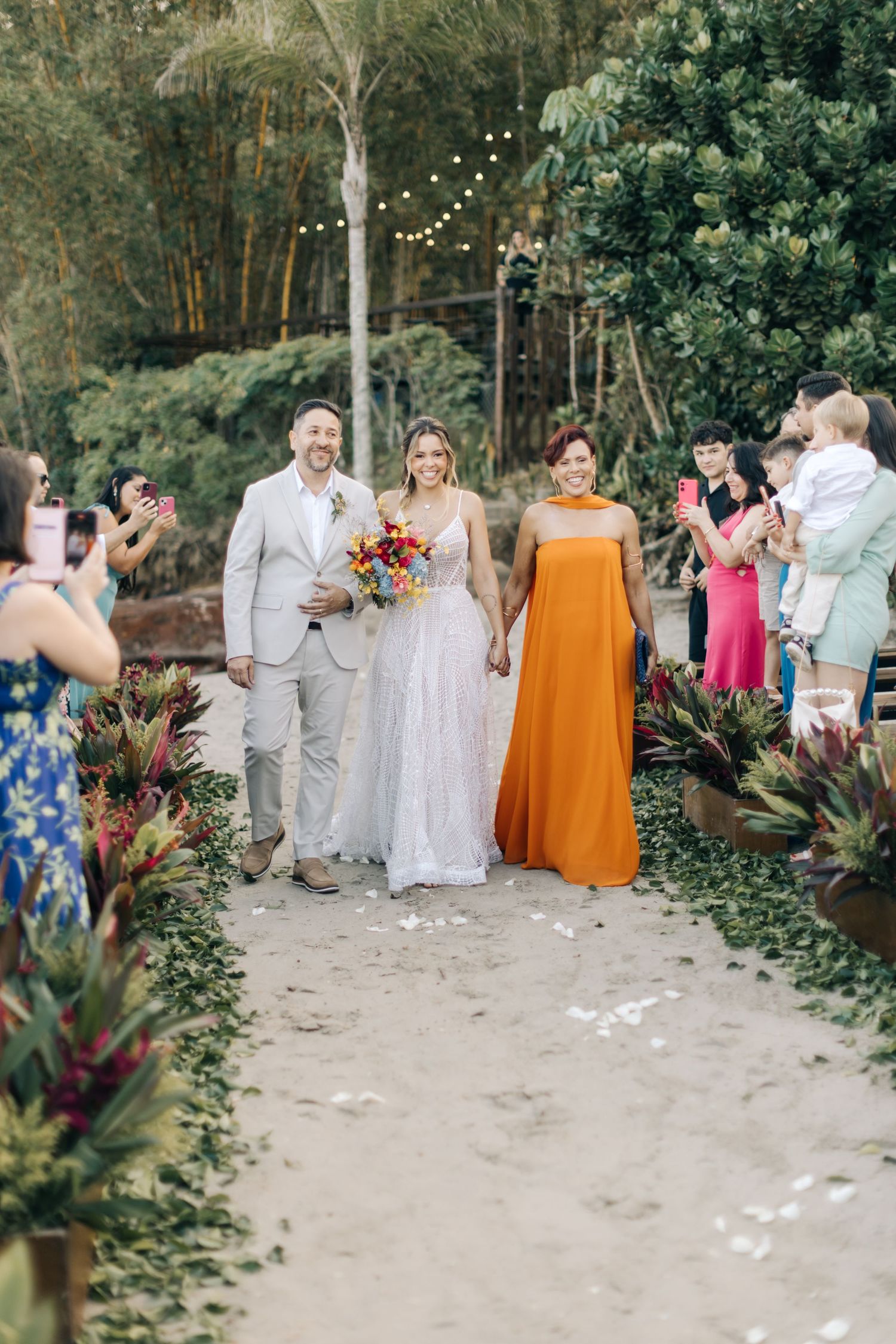 Wedding party and guests gathered on garden path with string lights overhead.