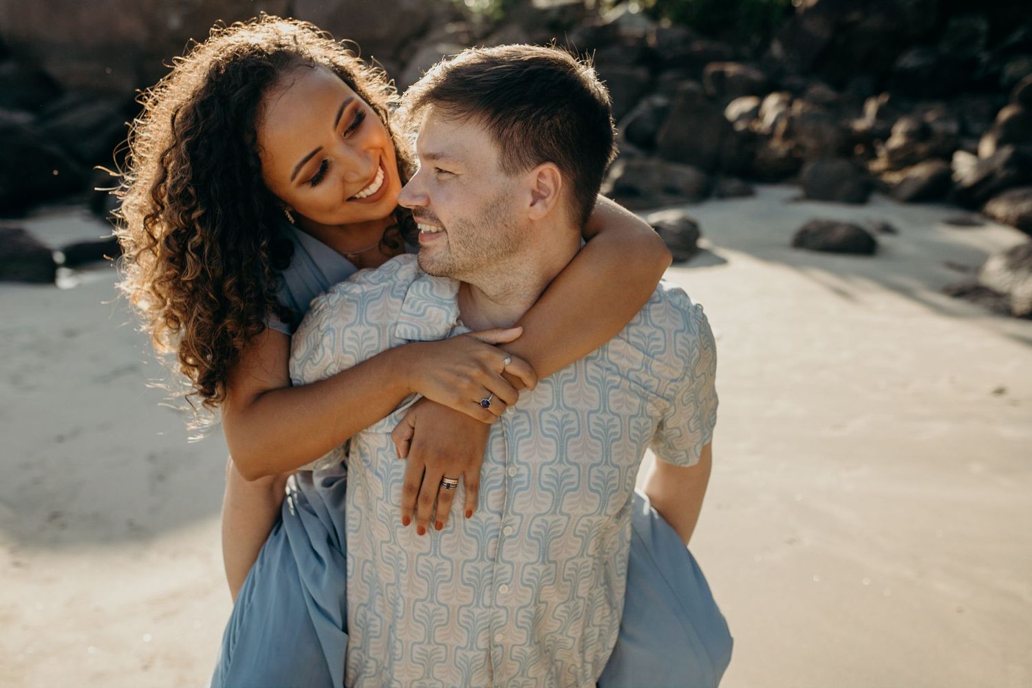 Intimate beach portrait of couple laughing together against coastal rocks.