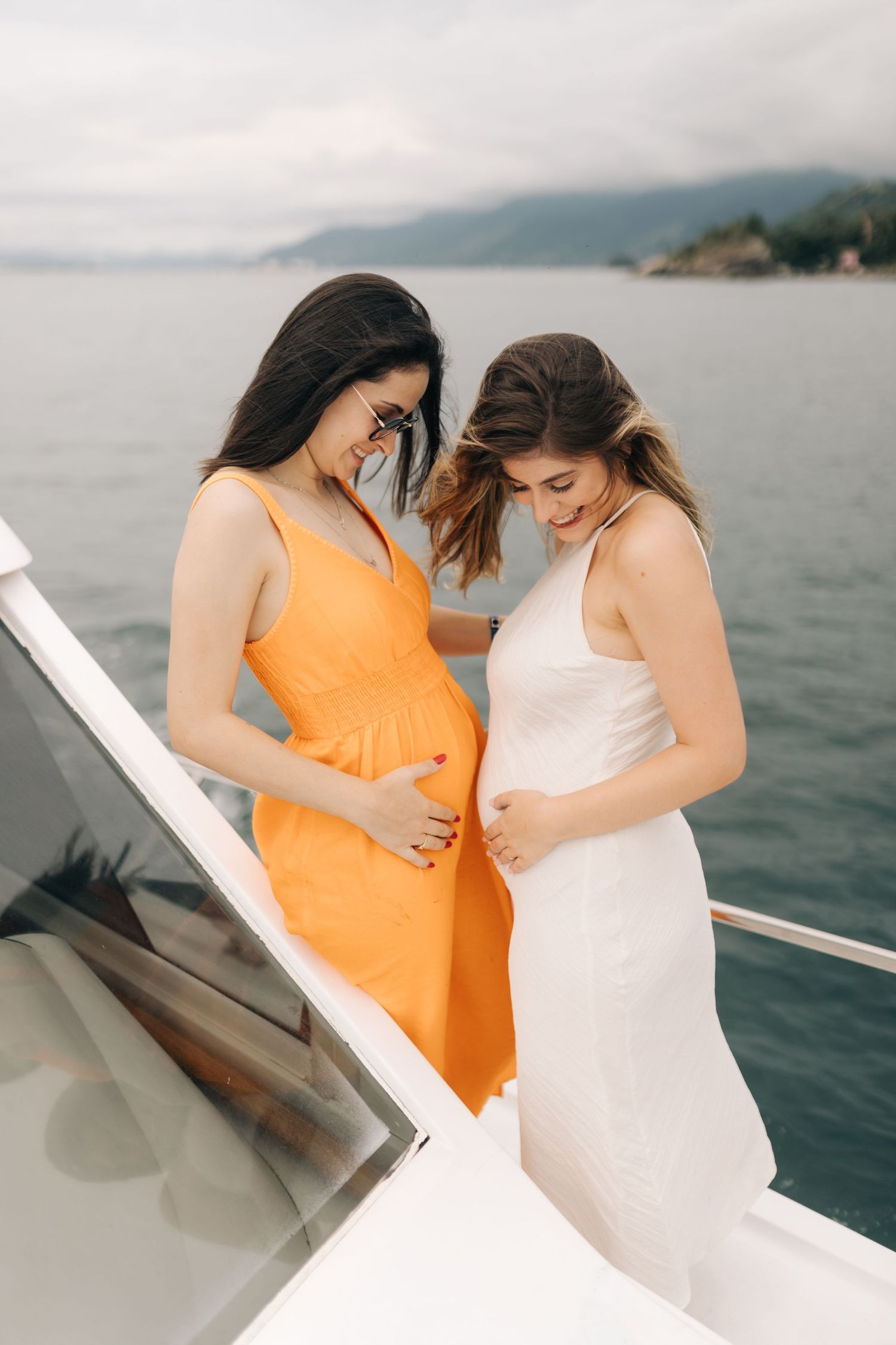 Friends in orange and white dresses having fun on a boat against coastal scenery.