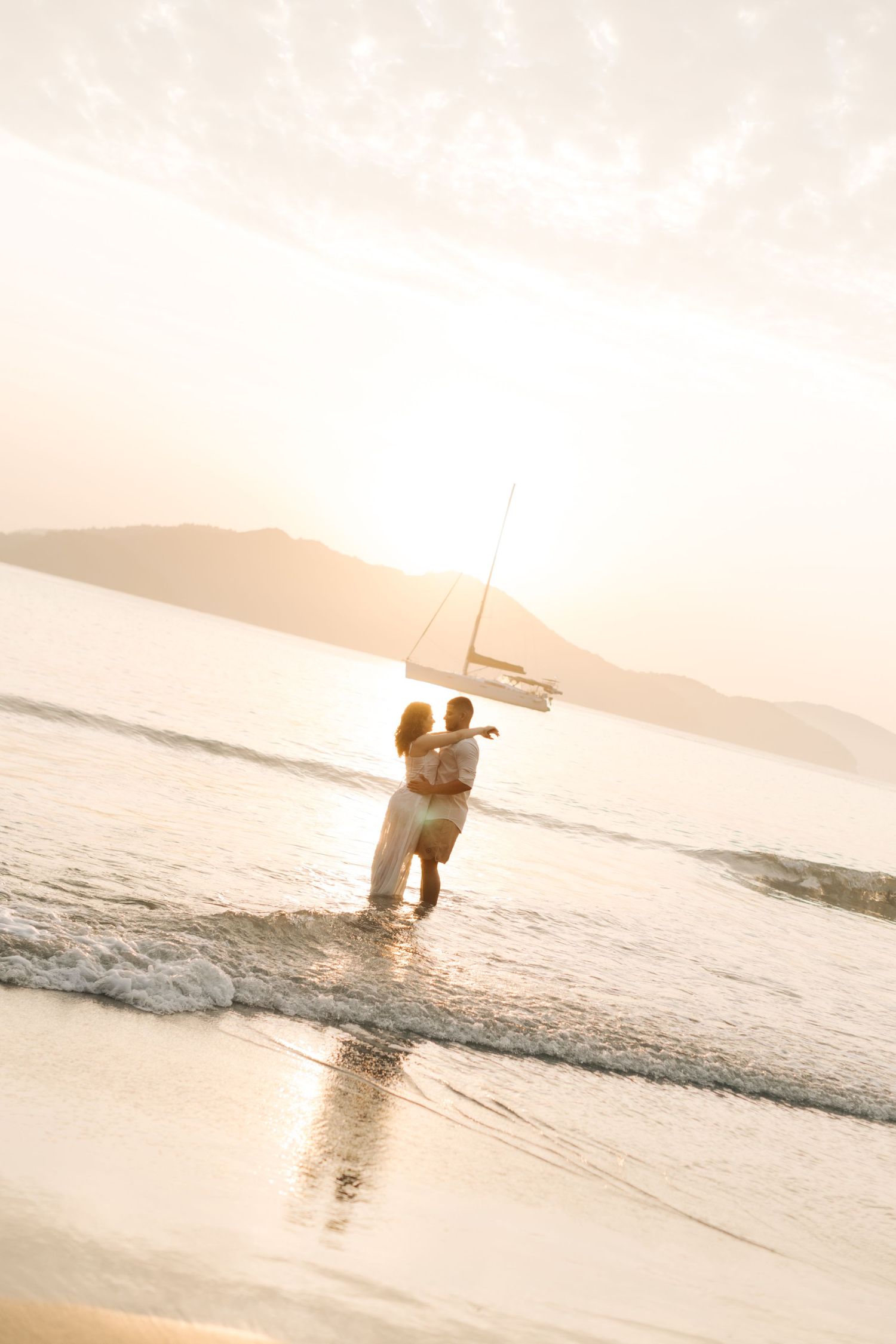 A romantic beach photoshoot with couple embracing in ocean waves at golden hour.