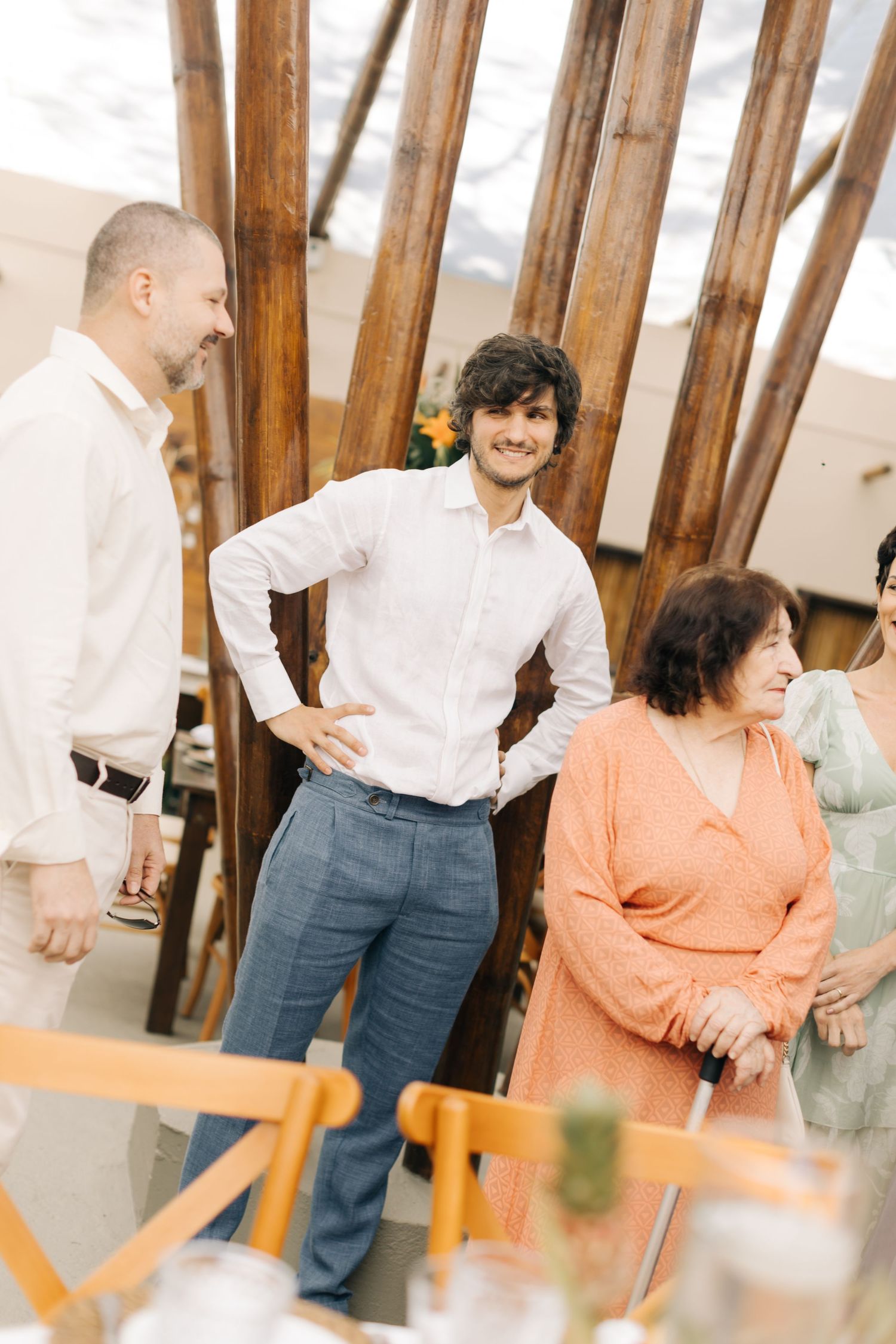 Casual gathering with people in white shirts and colorful attire near wooden beams.