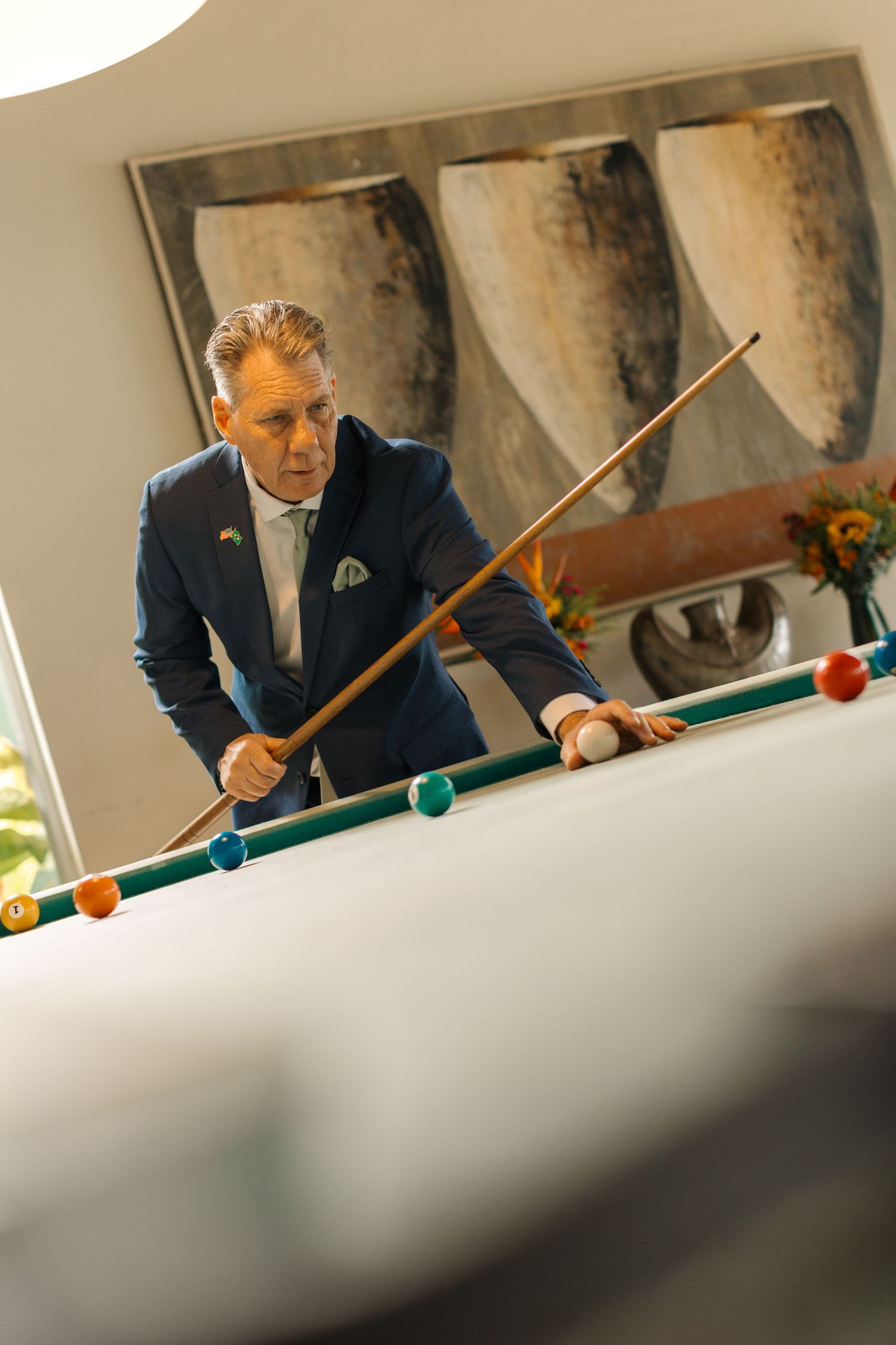 A person in a navy suit plays pool, focusing on lining up a shot on the green felt table.