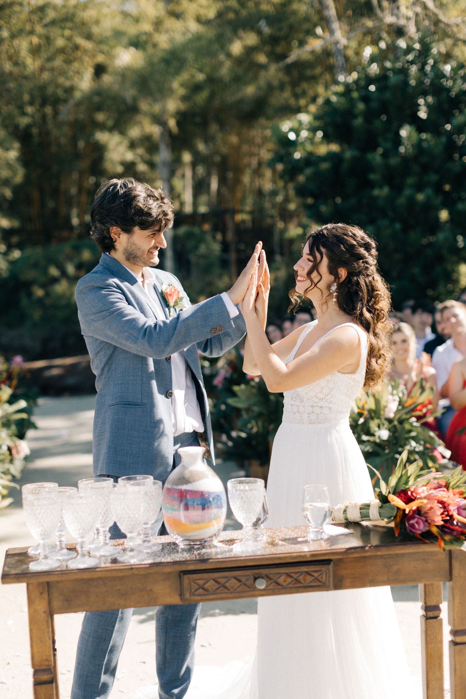 Wedding couple high-fives while mixing drinks at their outdoor reception bar.