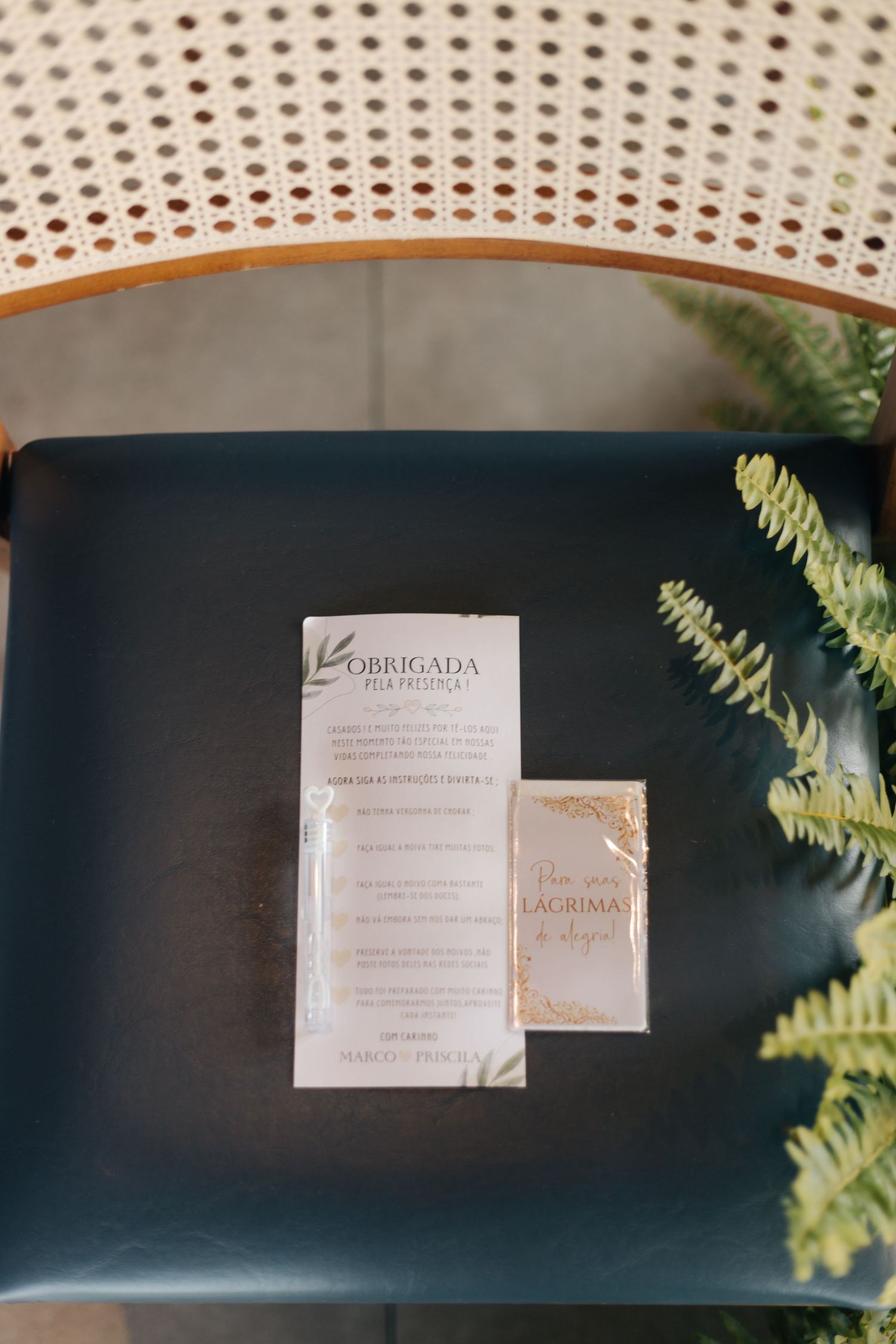 Wedding invitation card displayed on a dark chair with ferns in the background.