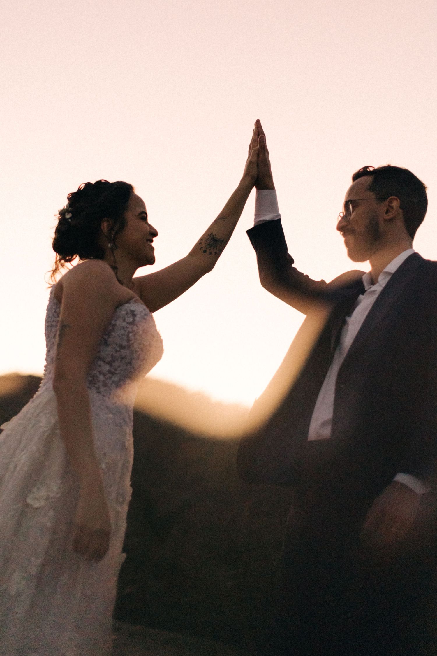 Newlyweds share a high-five celebration against a sunset sky.