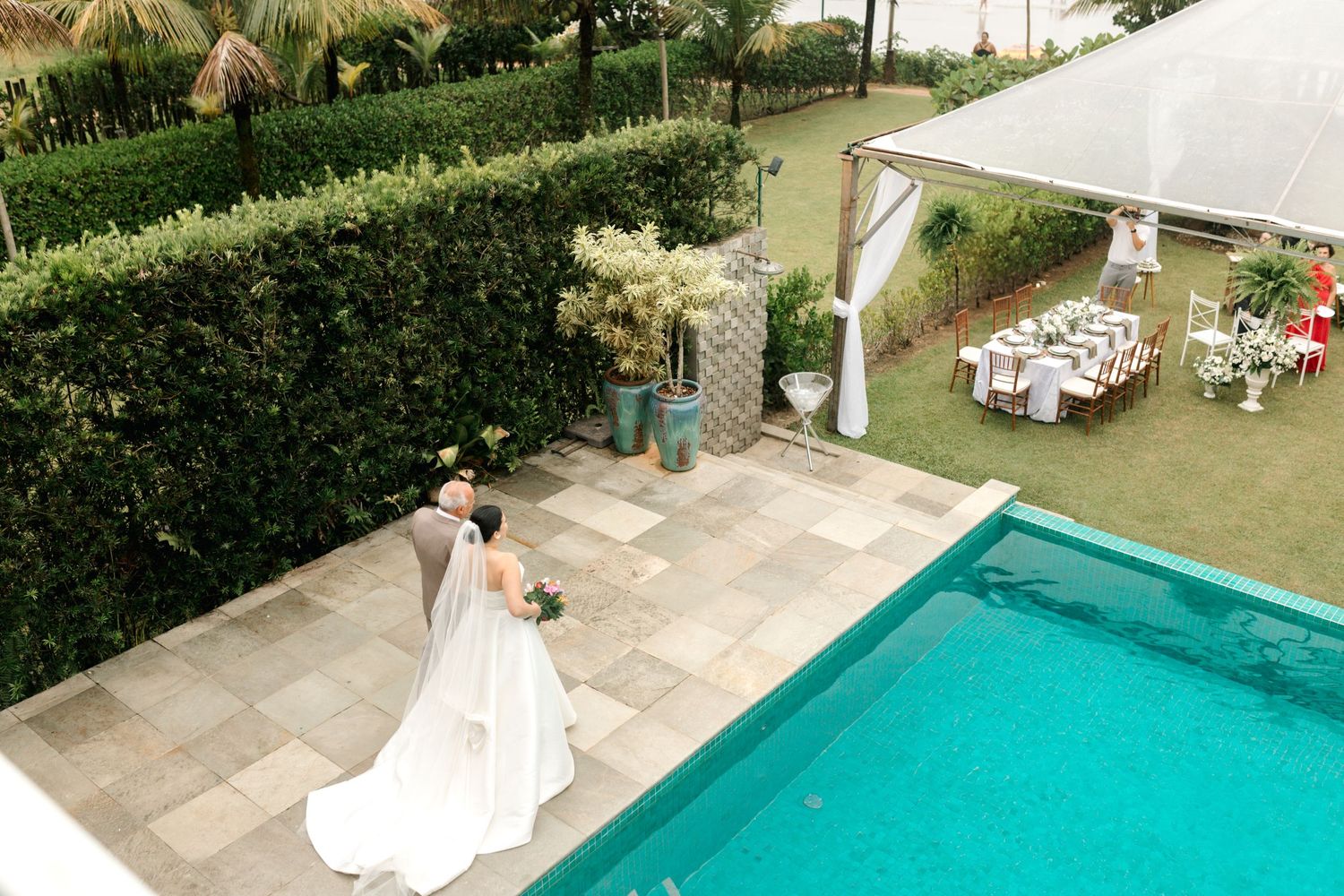 A beautiful outdoor wedding ceremony setting with a pool and lush greenery in the background.