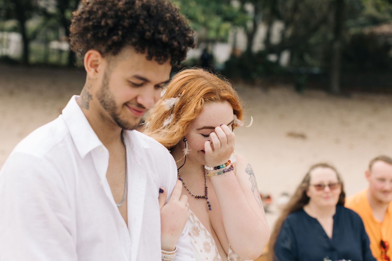 Emotional wedding moment captured on a sandy beach with guests in background.