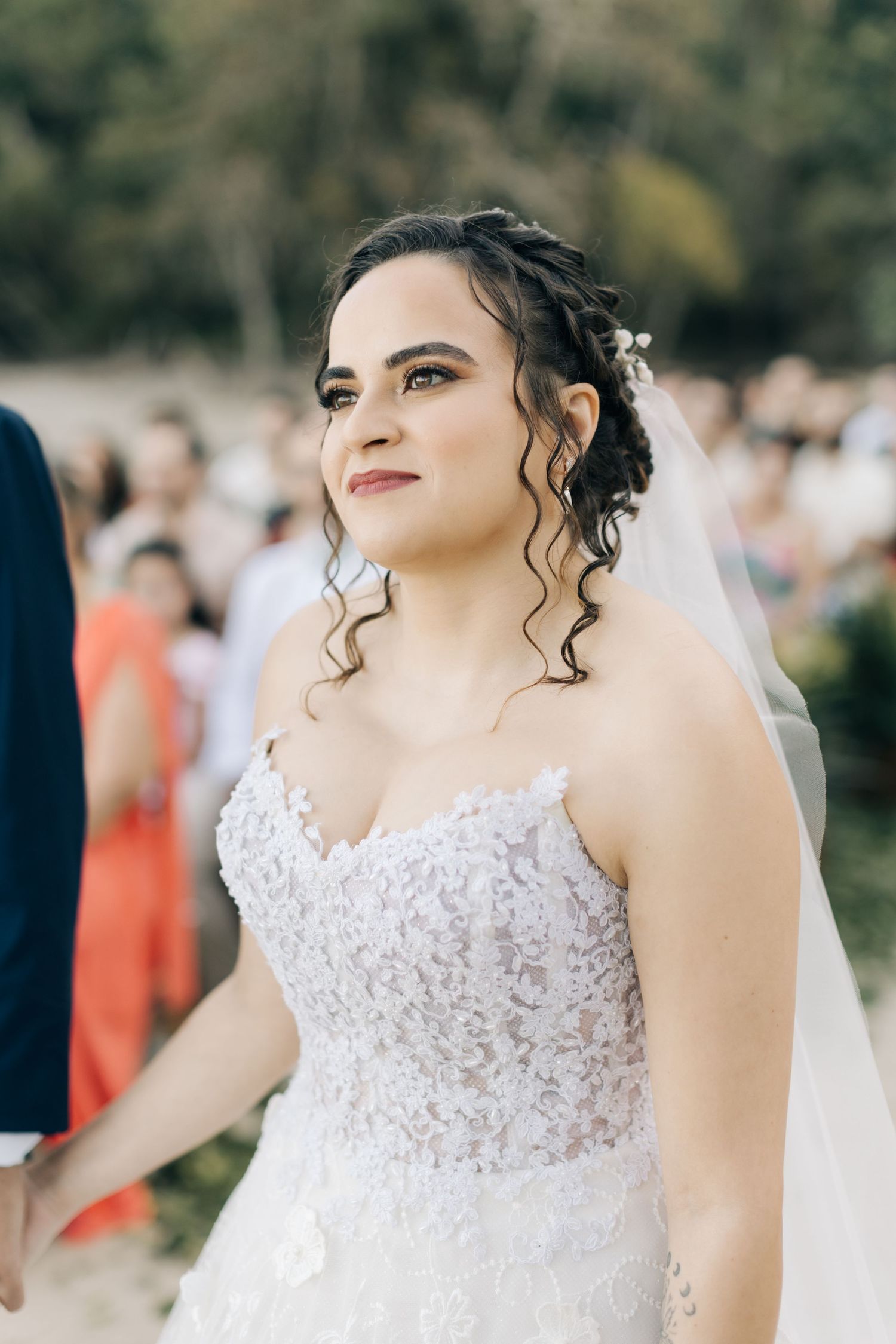 Side profile of bride in detailed lace wedding dress during outdoor ceremony.