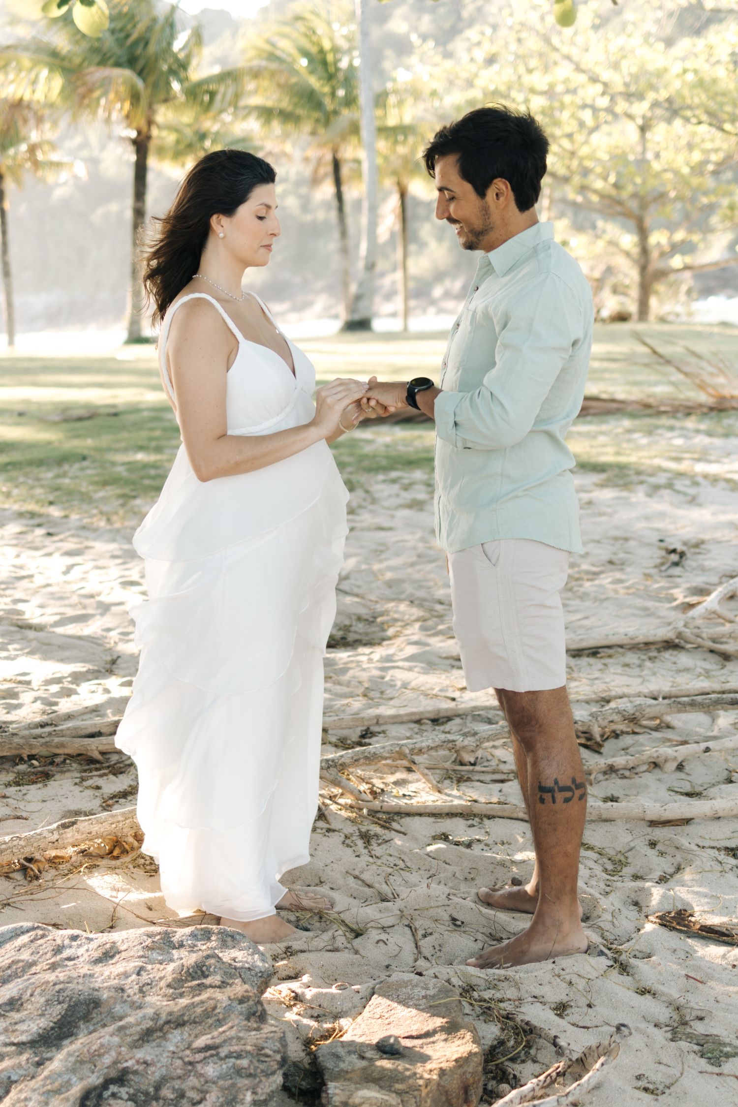 A couple in white outfits playfully dancing together on a sandy beach during a photo session.