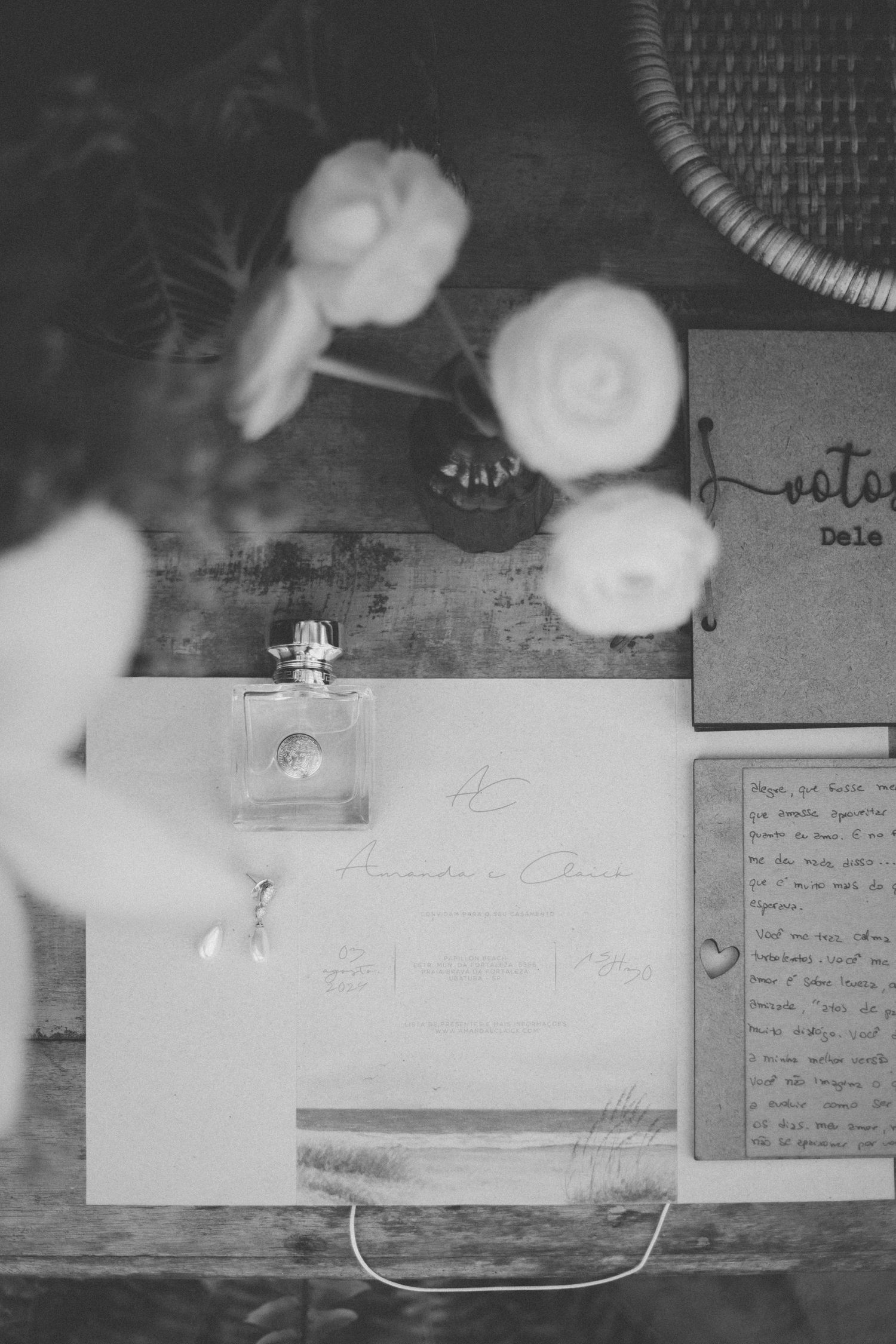 Black and white photo of wedding stationery with perfume bottle on wooden surface.