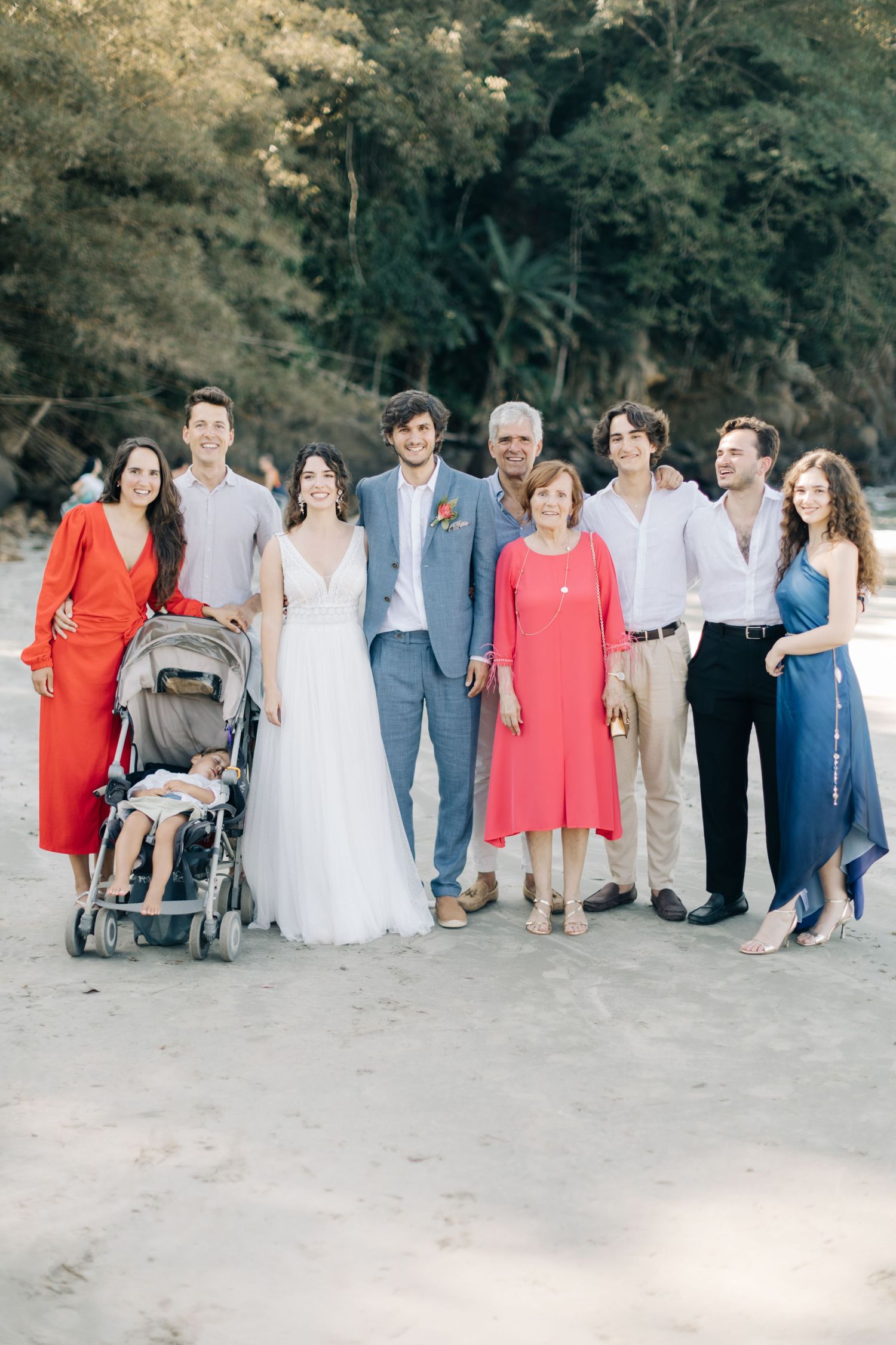 Wedding group photo showing family and friends in coral and blue outfits on a sandy beach.