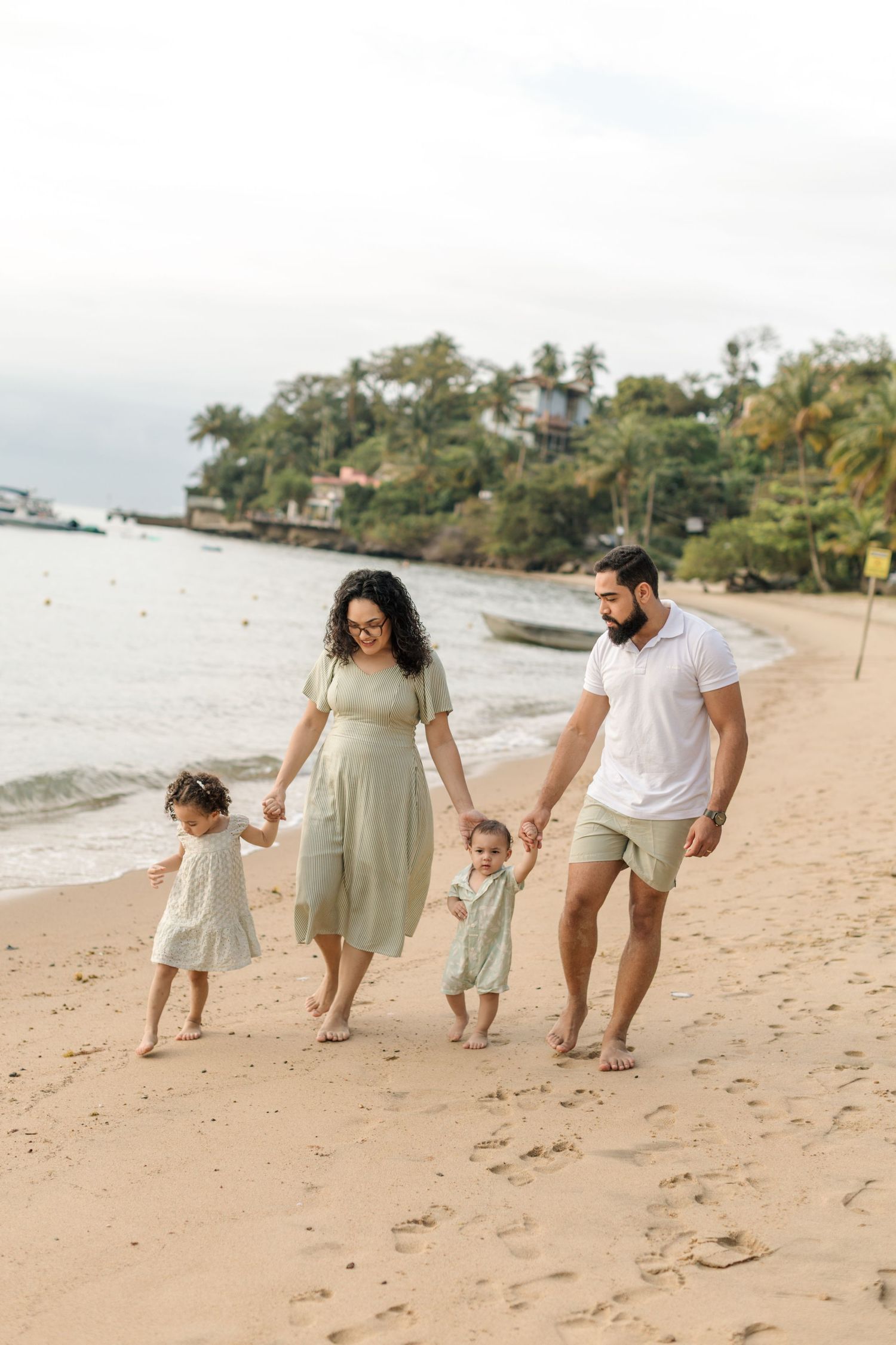 Family walking together holding hands on a tropical beach with palm trees in the background.