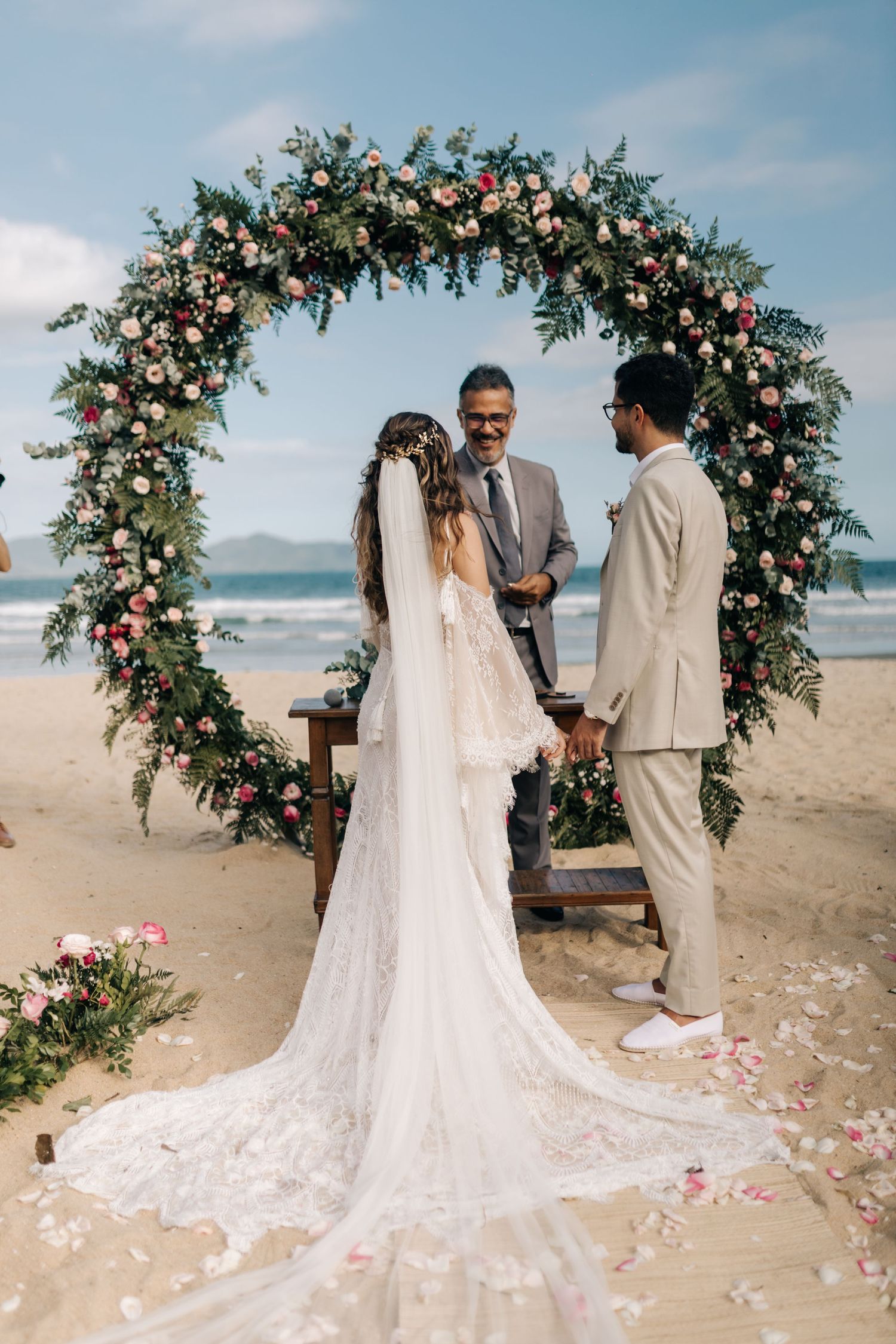 A wedding ceremony in progress under an elaborate flower arch with a long train dress.