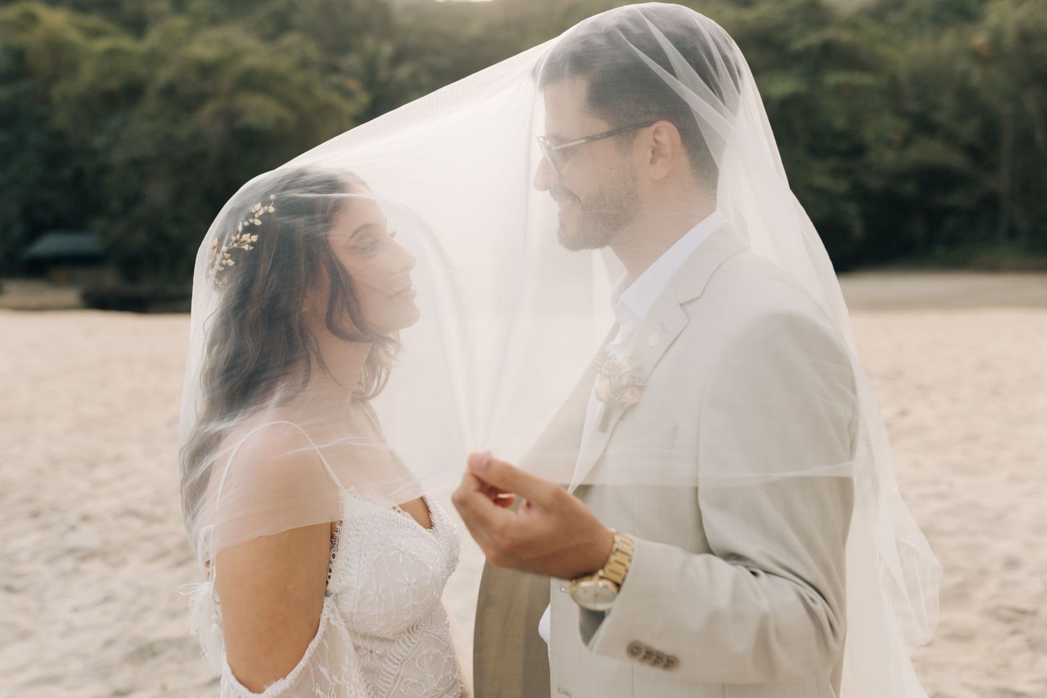 A romantic beach wedding moment under a flowing veil as the couple shares an intimate moment during sunset.