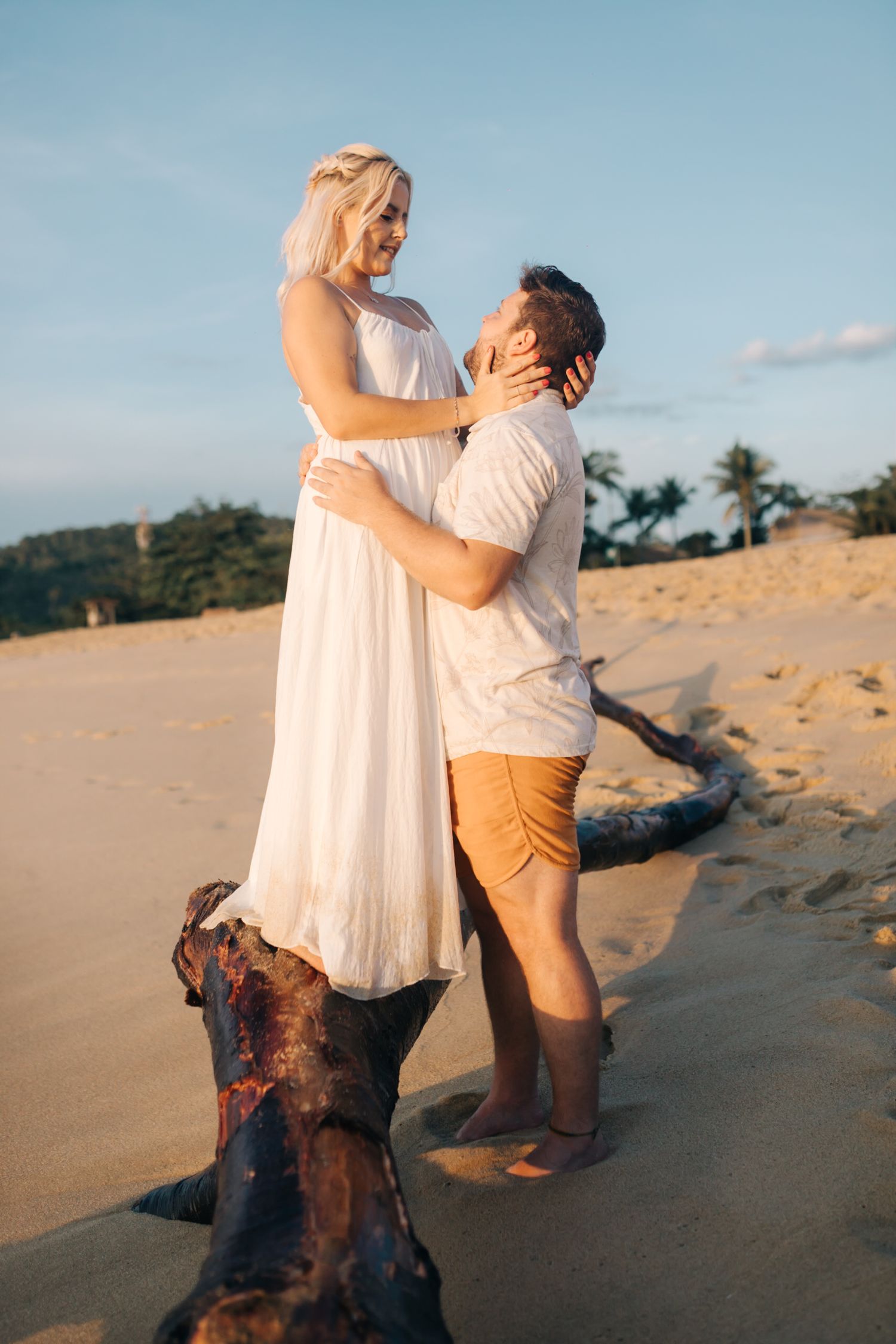 A romantic beach moment captured between two people near driftwood at sunset.