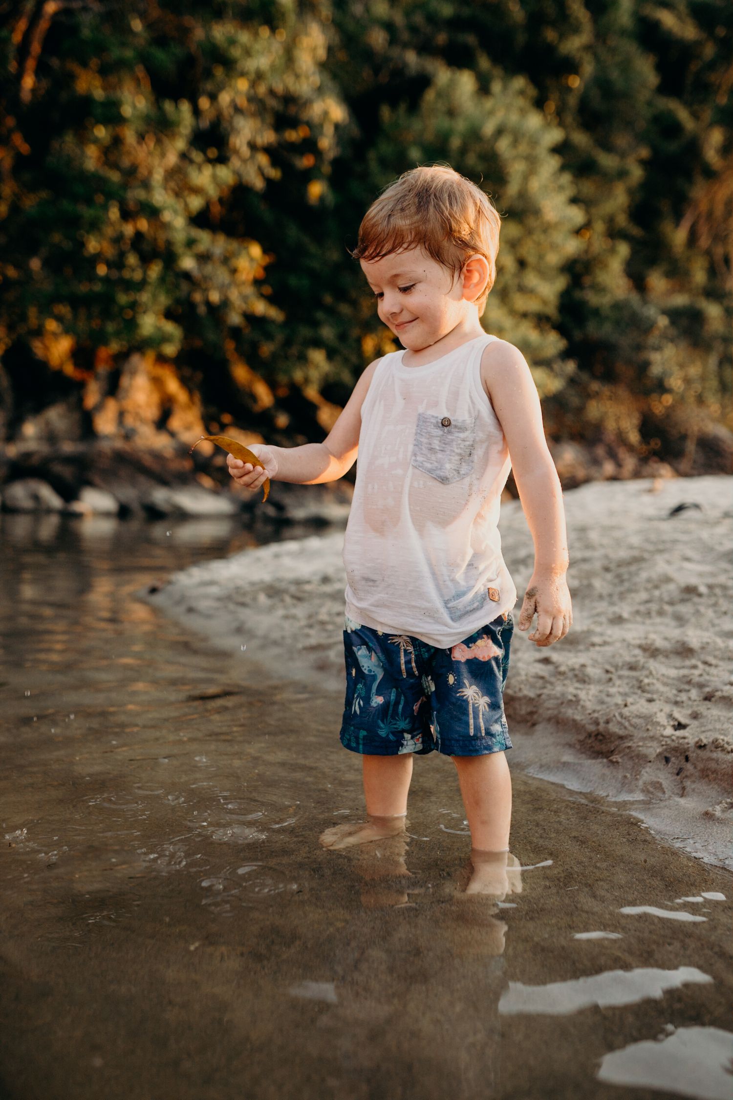 Young child splashing and playing in shallow beach water near rocky shore.
