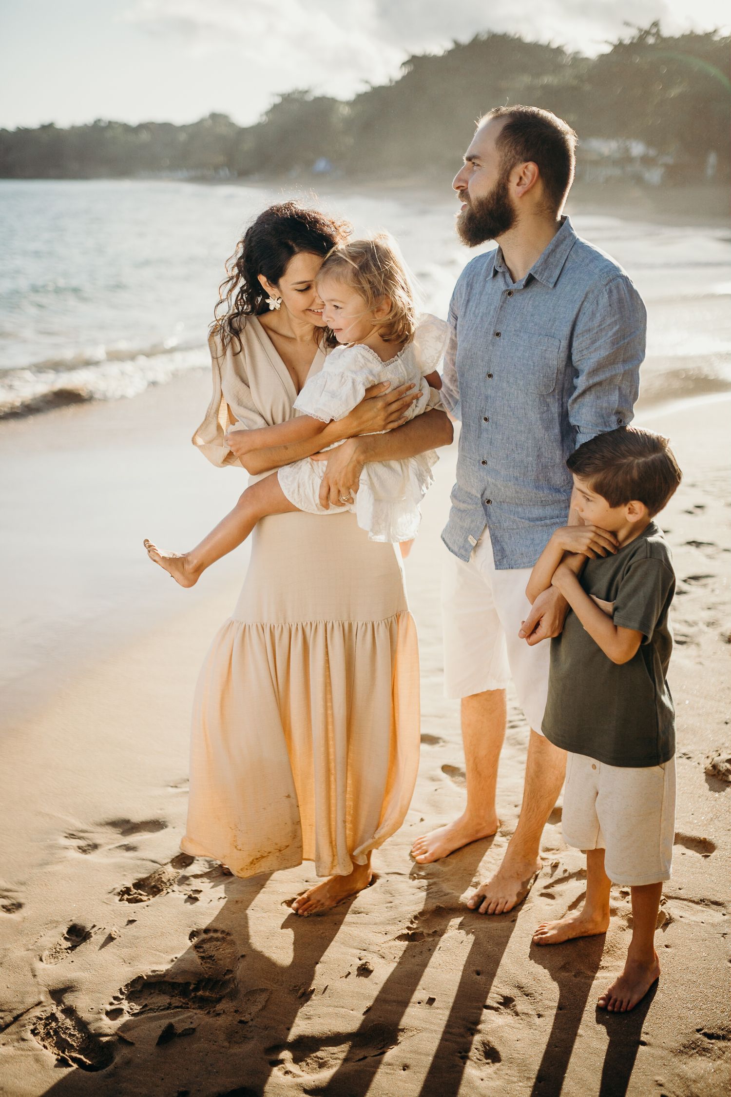 A family stands together on a beach during golden hour creating long shadows.