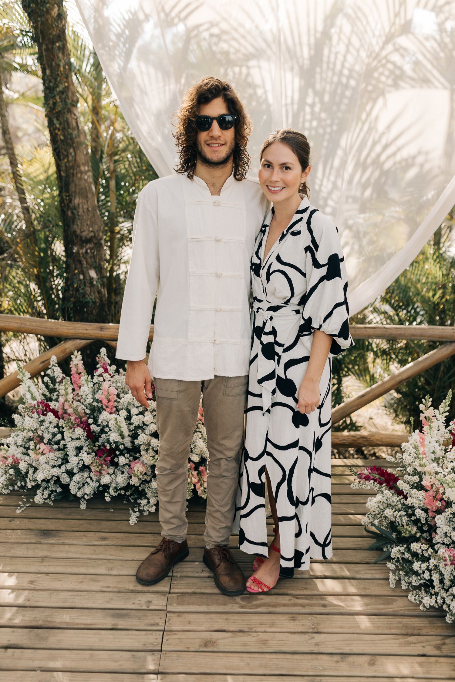 Couple in coordinating black and white outfits pose on wooden deck with floral decorations.