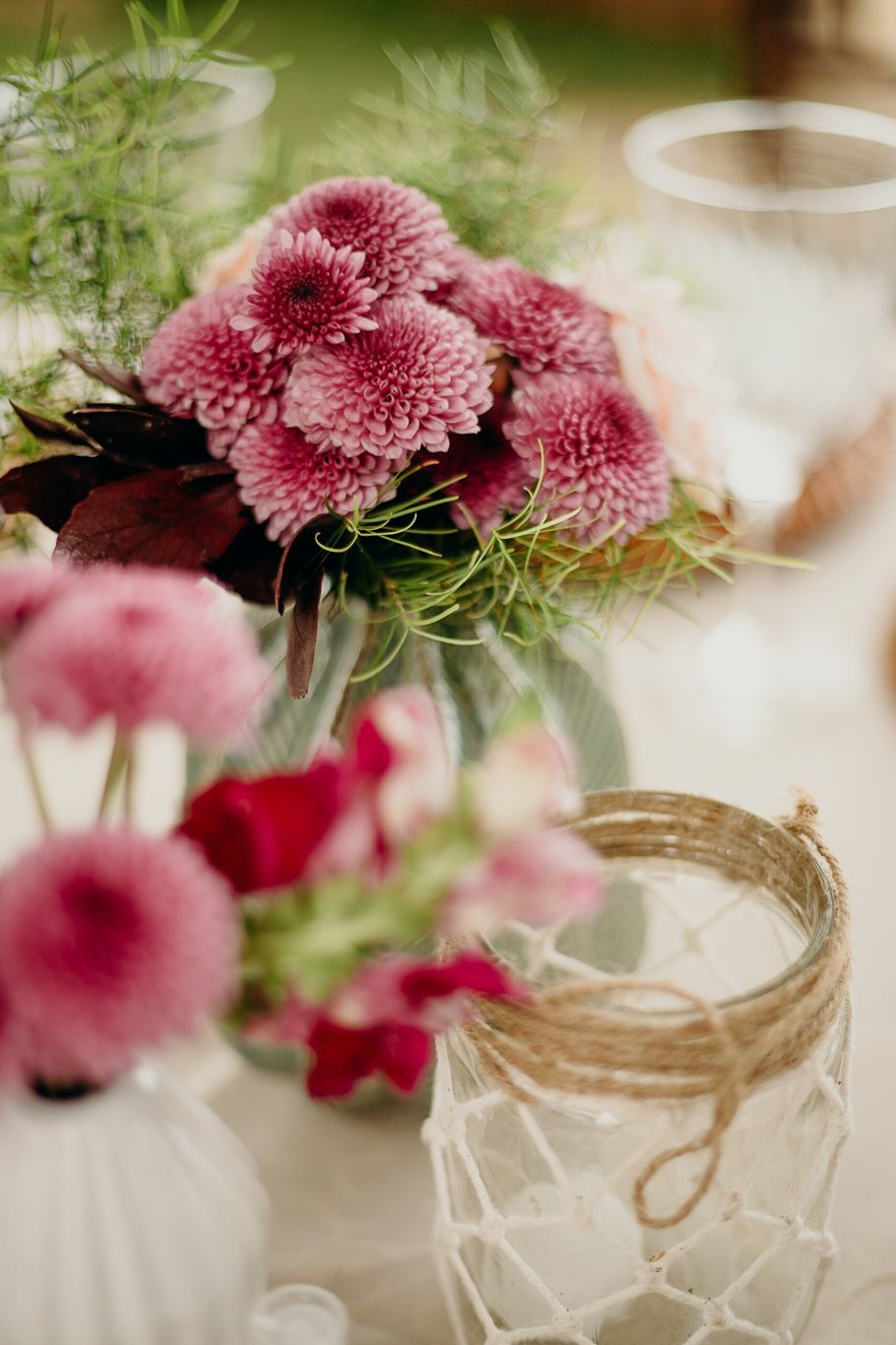 Pink chrysanthemums and delicate greenery arranged in a mason jar wrapped with twine.