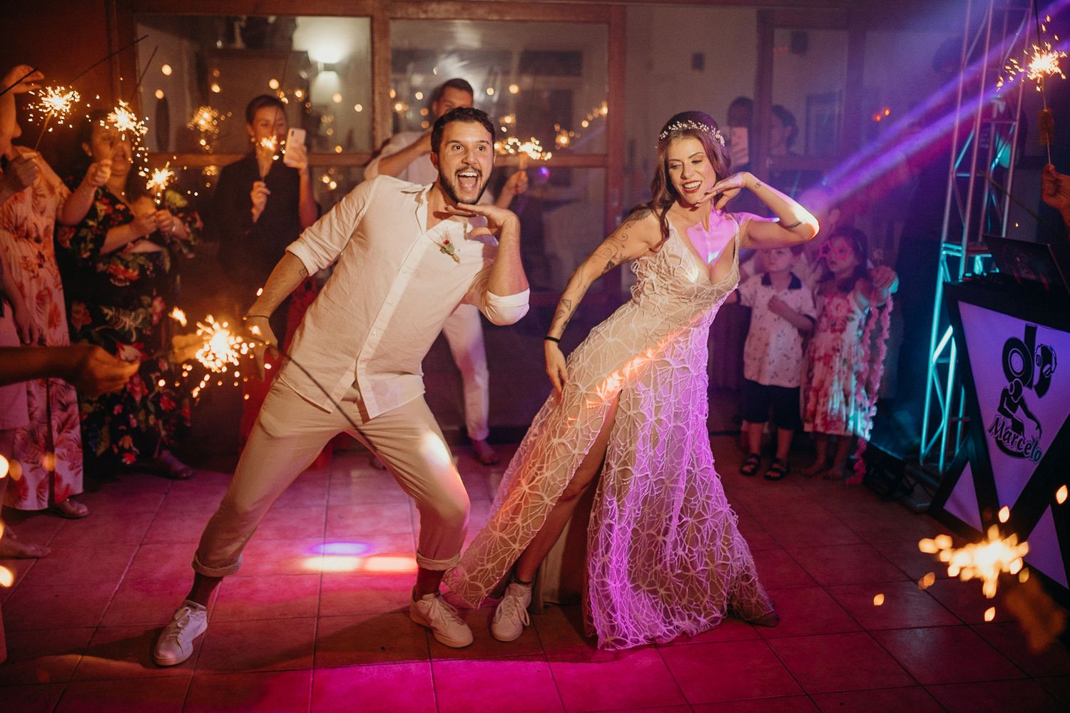 Energetic dance moves captured during a wedding reception with purple lighting and sparklers.
