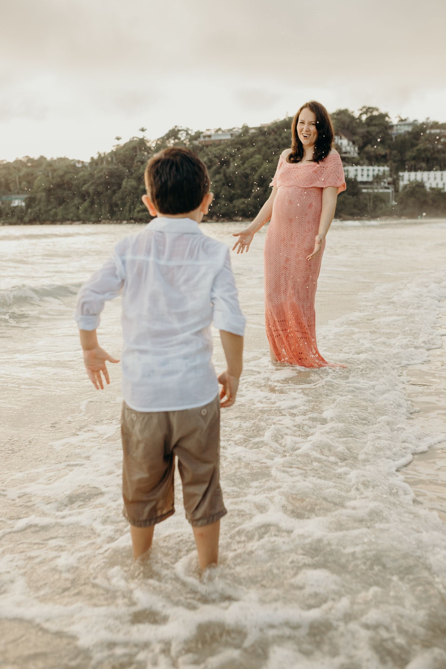 Two people standing in gentle waves on a scenic beach at sunset.