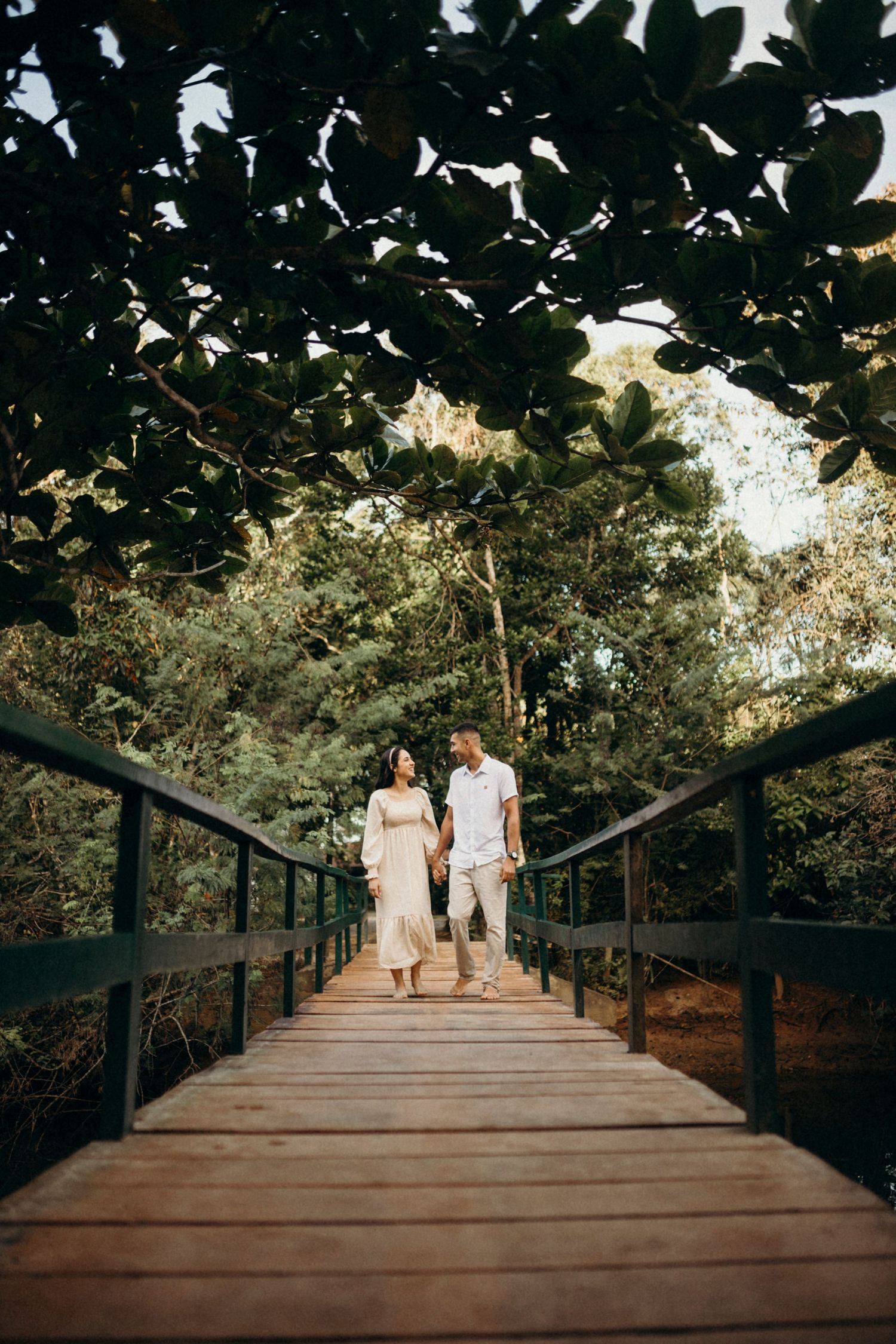 Long wooden boardwalk through nature with couple in white walking together.