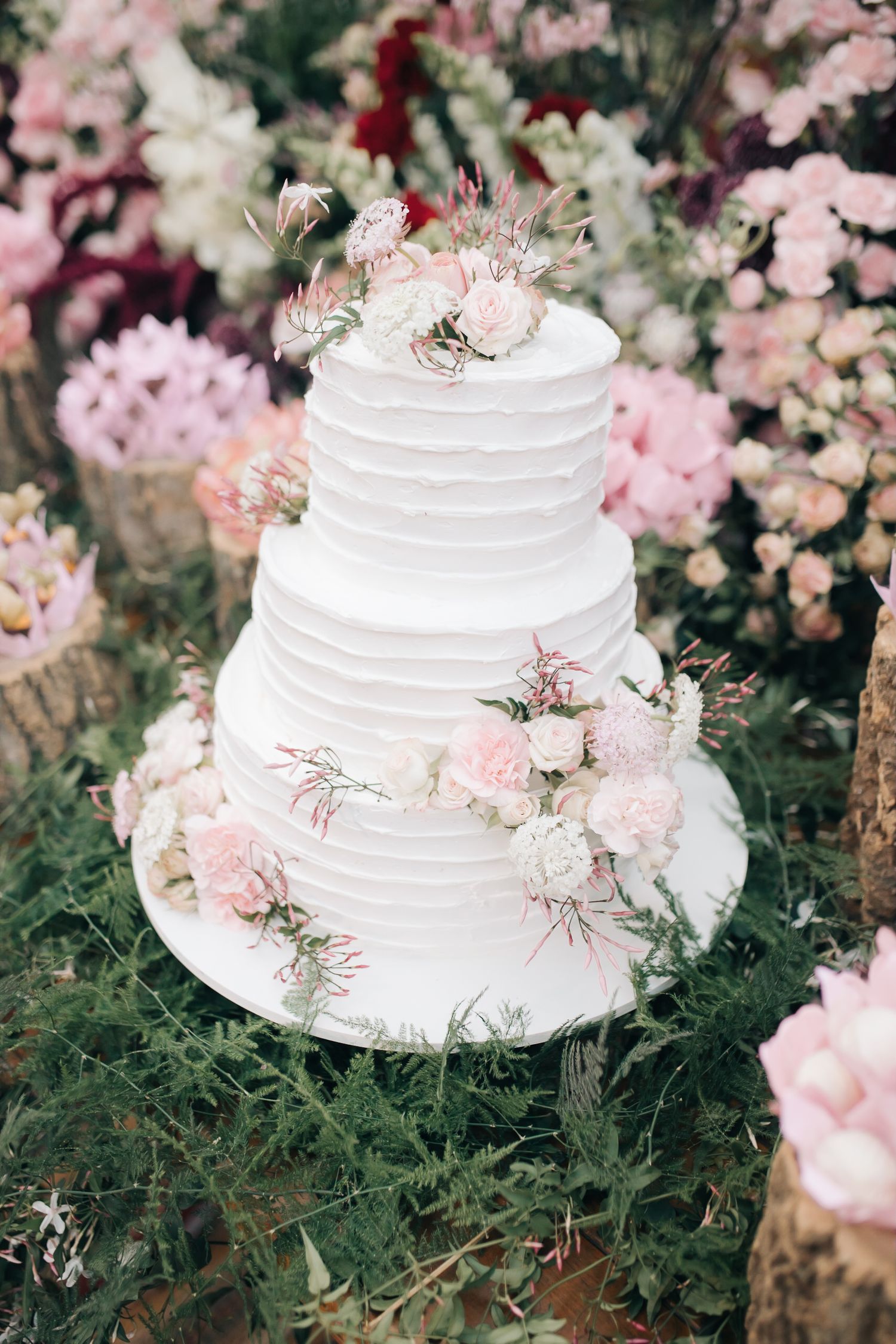 White tiered wedding cake decorated with delicate pink and blush florals against floral background.