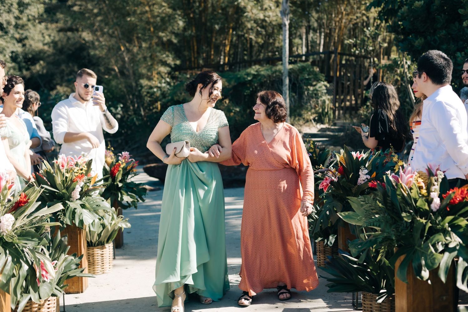 Bridal party in coordinated mint and coral dresses standing near lush tropical decor.