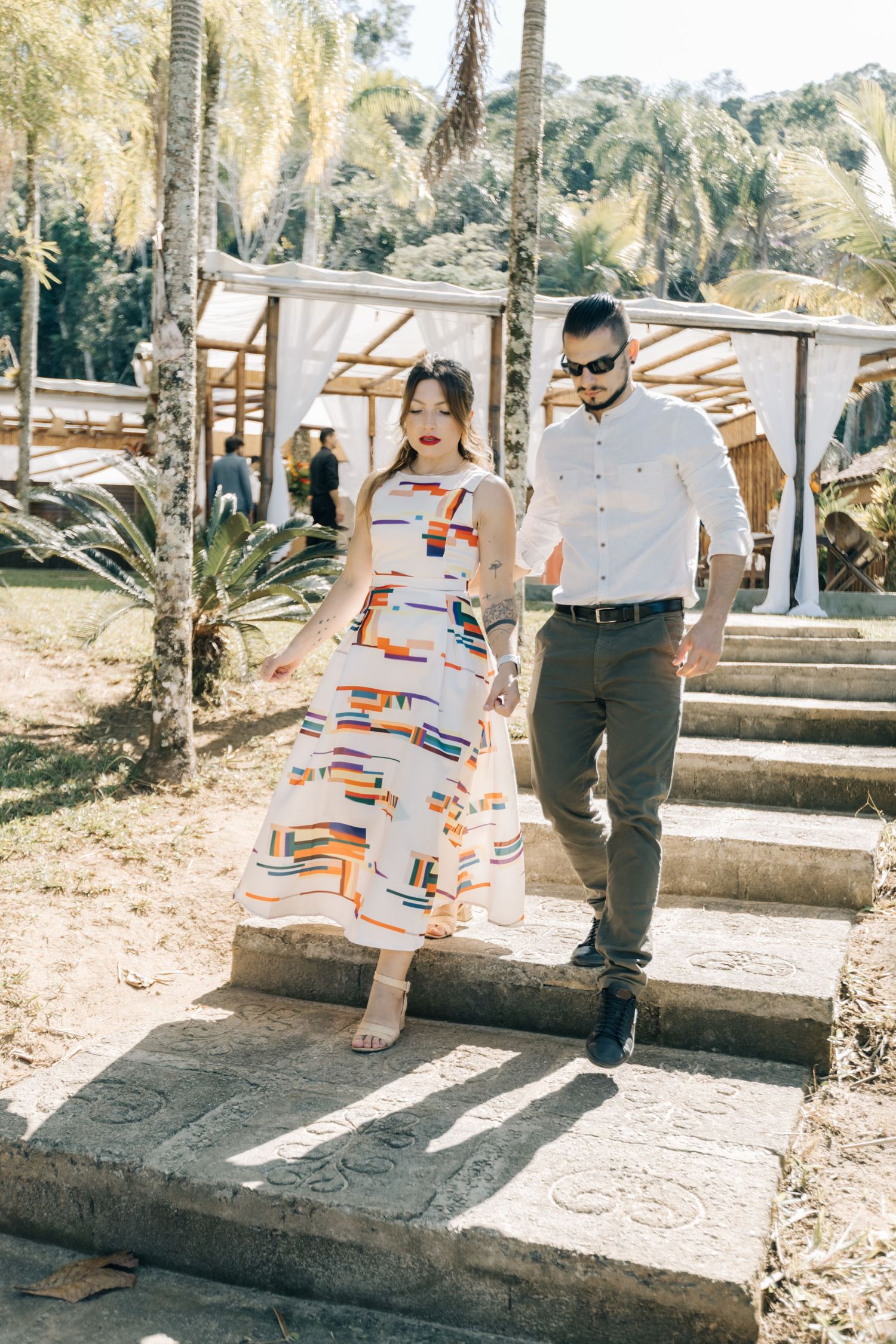 Couple walking down stone steps at tropical resort with palm trees.