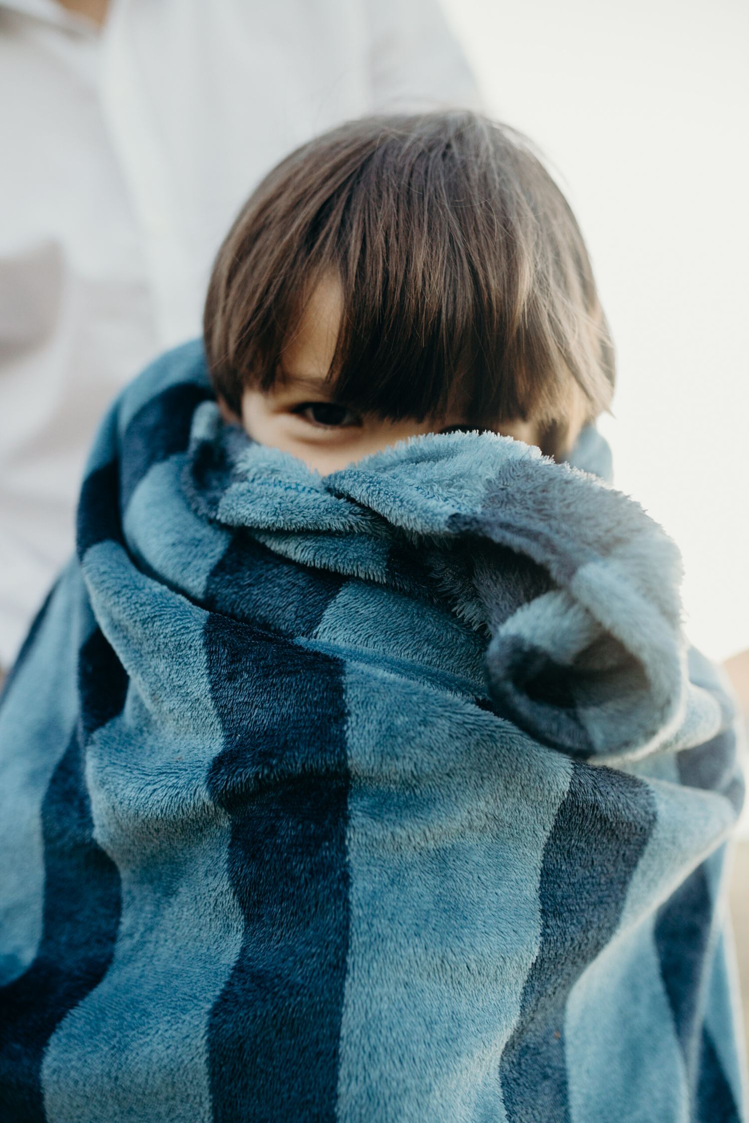 Close-up view of someone partially hidden behind a blue striped beach towel.