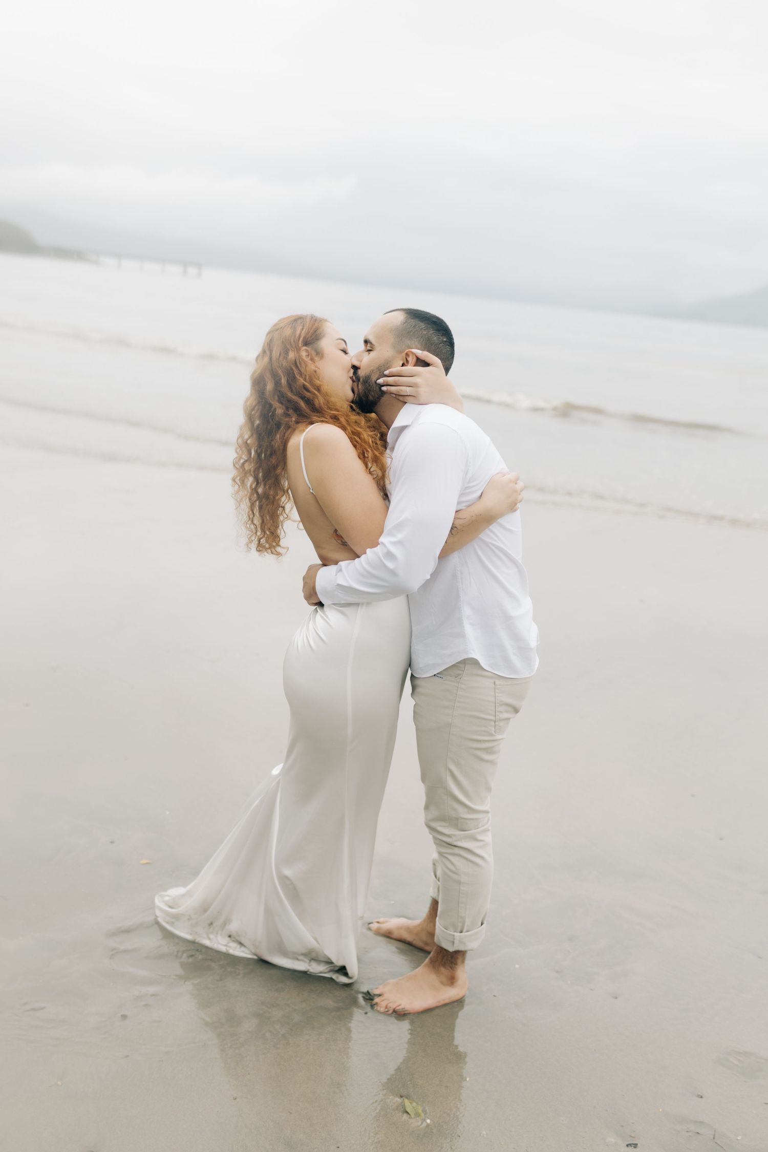 Romantic embrace between couple on cloudy beach during engagement photos.