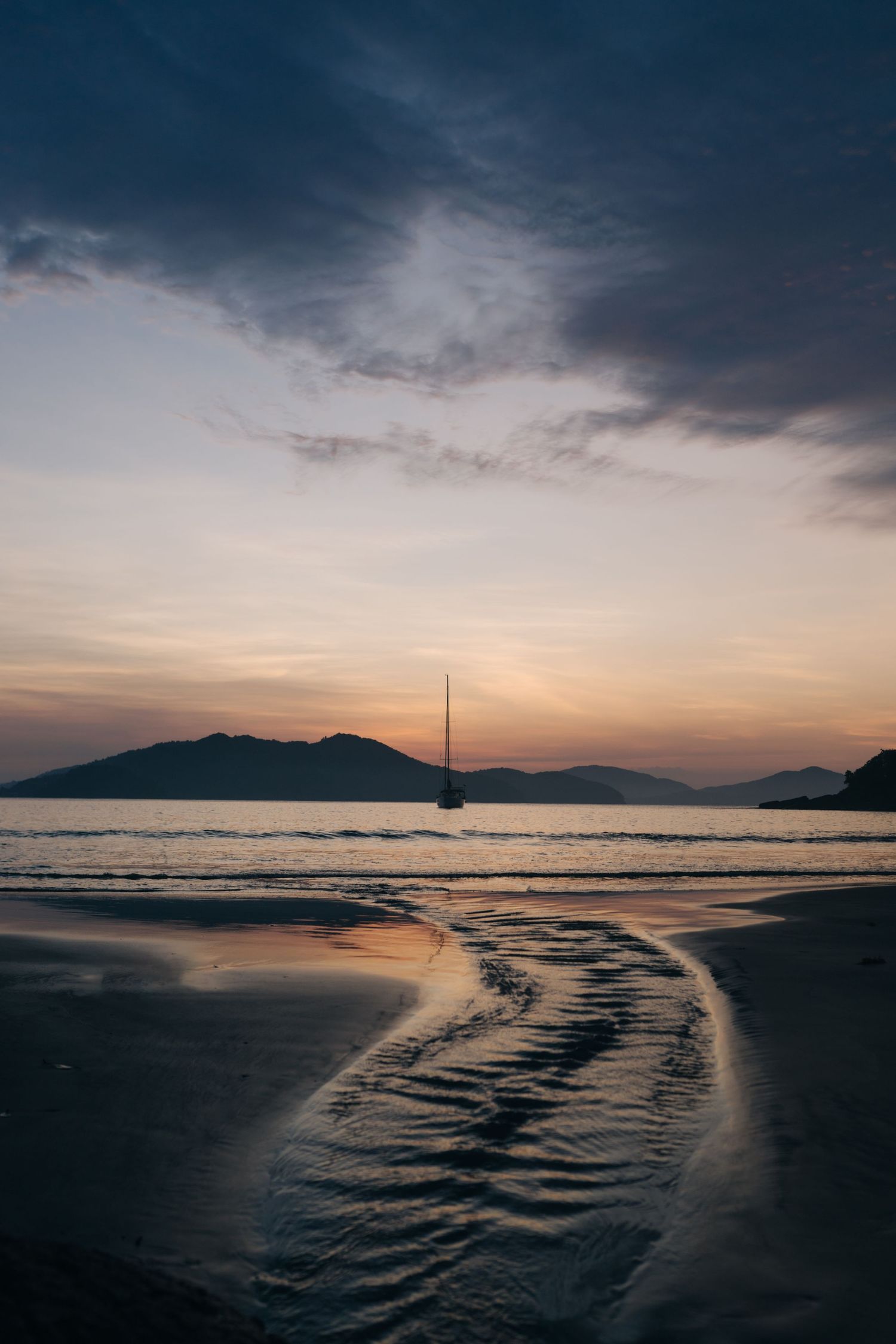 Dramatic sunset seascape with rippled sand patterns and distant mountains.