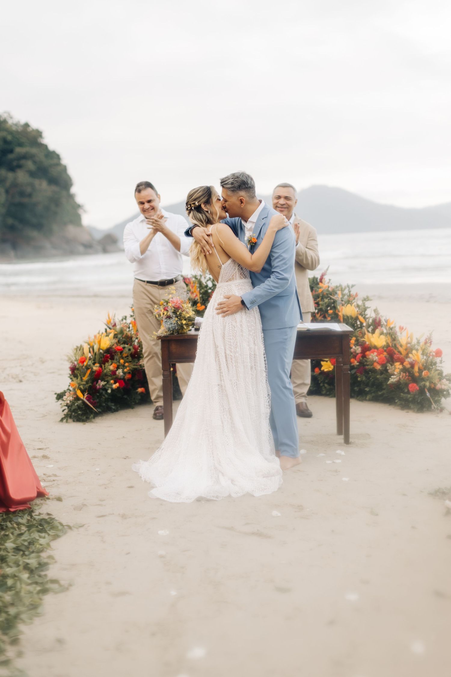 Joyful beach wedding celebration with sunset mountain backdrop and floral arrangements.